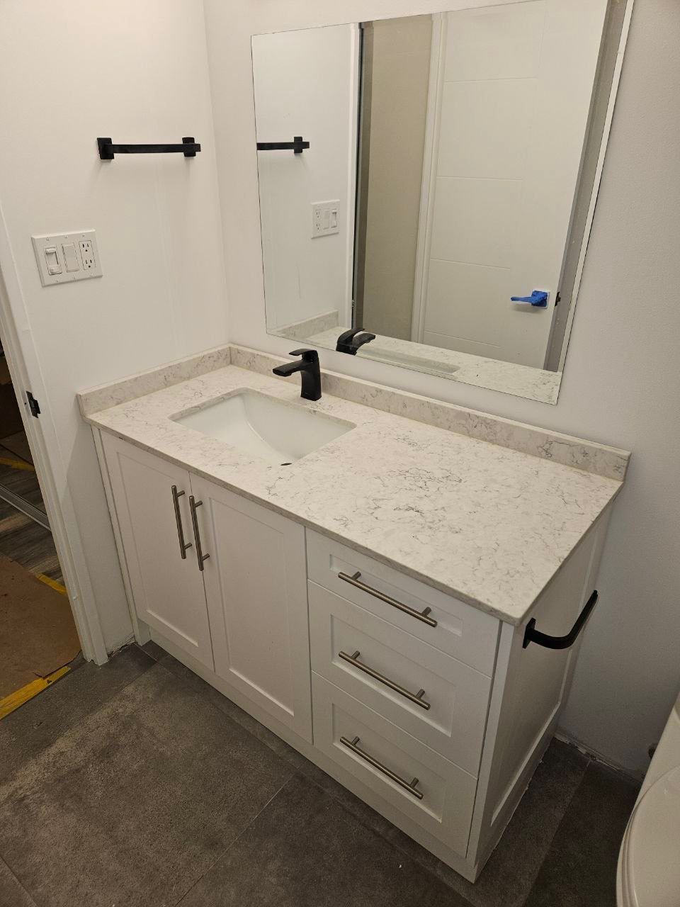Modern white vanity with quartz countertop and matte black faucet in a freshly renovated bathroom