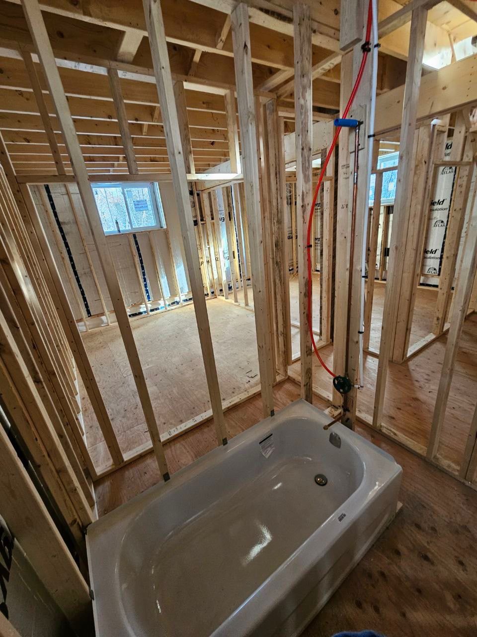 Framed bathroom with installed bathtub and exposed red PEX pipe