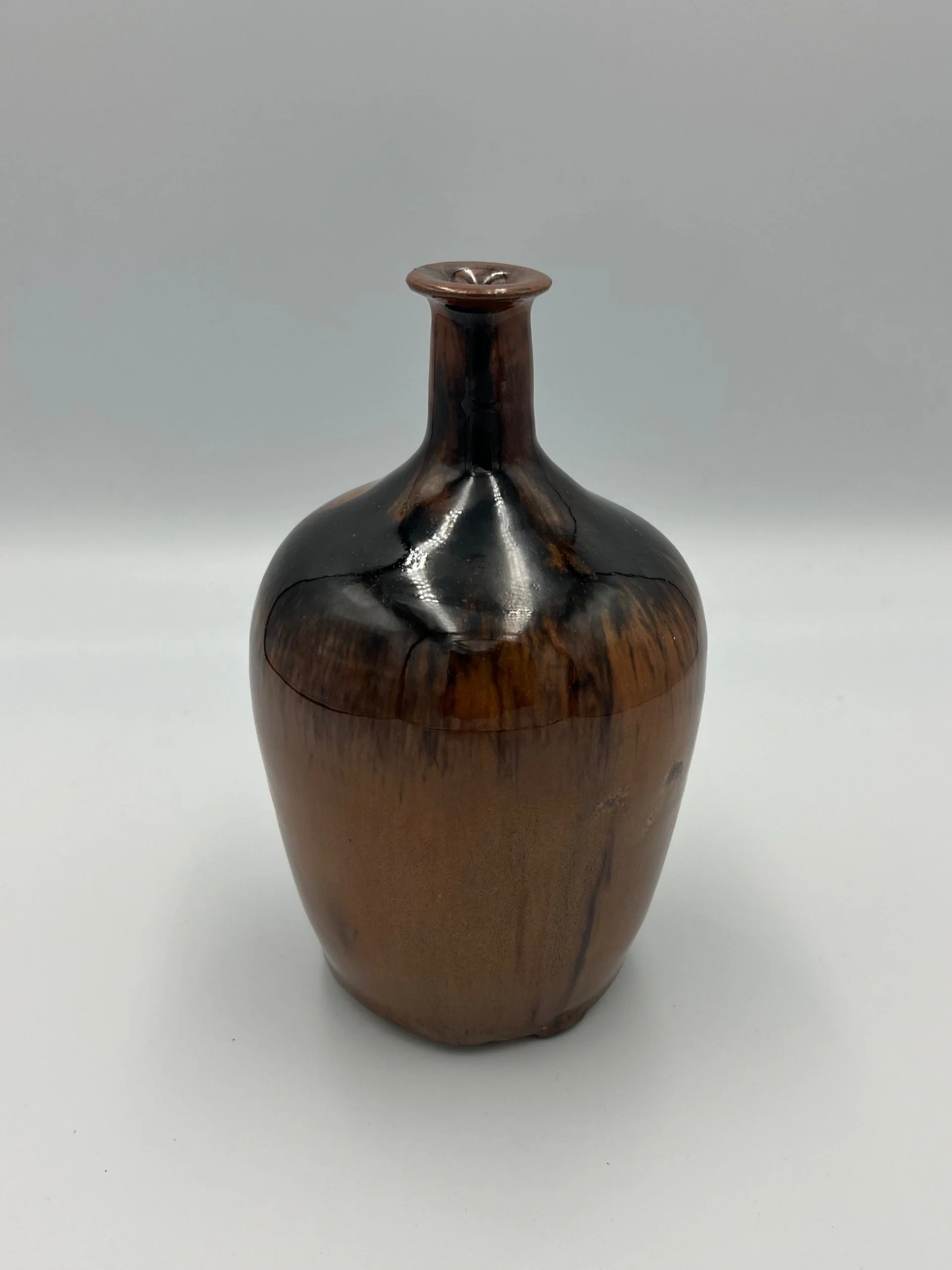 A glossy wooden vase with a narrow neck and a wide body, brown in color with darker streaks.