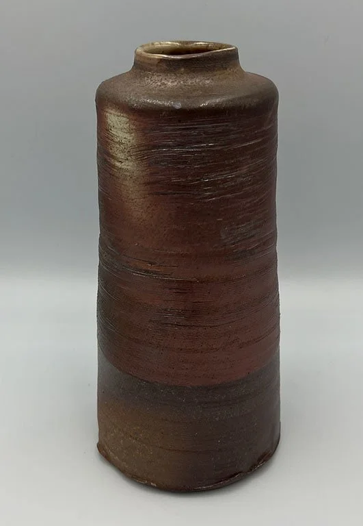 A tall, cylindrical, handmade ceramic vase with a earthy brown glaze and textured horizontal lines.