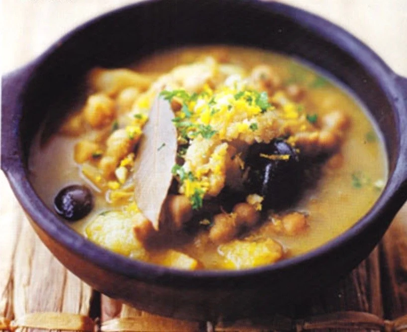 A bowl of yellow lentil soup garnished with herbs, spices, and a bay leaf.