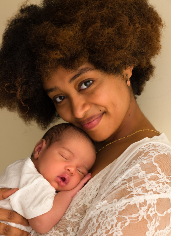 A woman with curly hair holding a sleeping baby close to her chest.