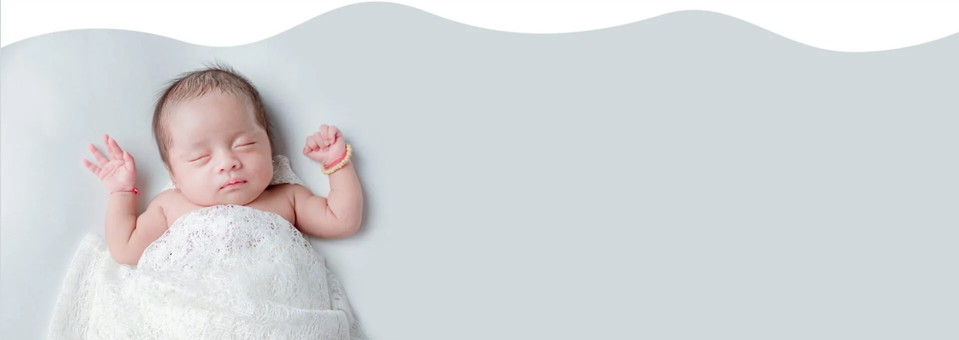 baby sleeping on back with arms above their head wrapped in a white gauze blanket.