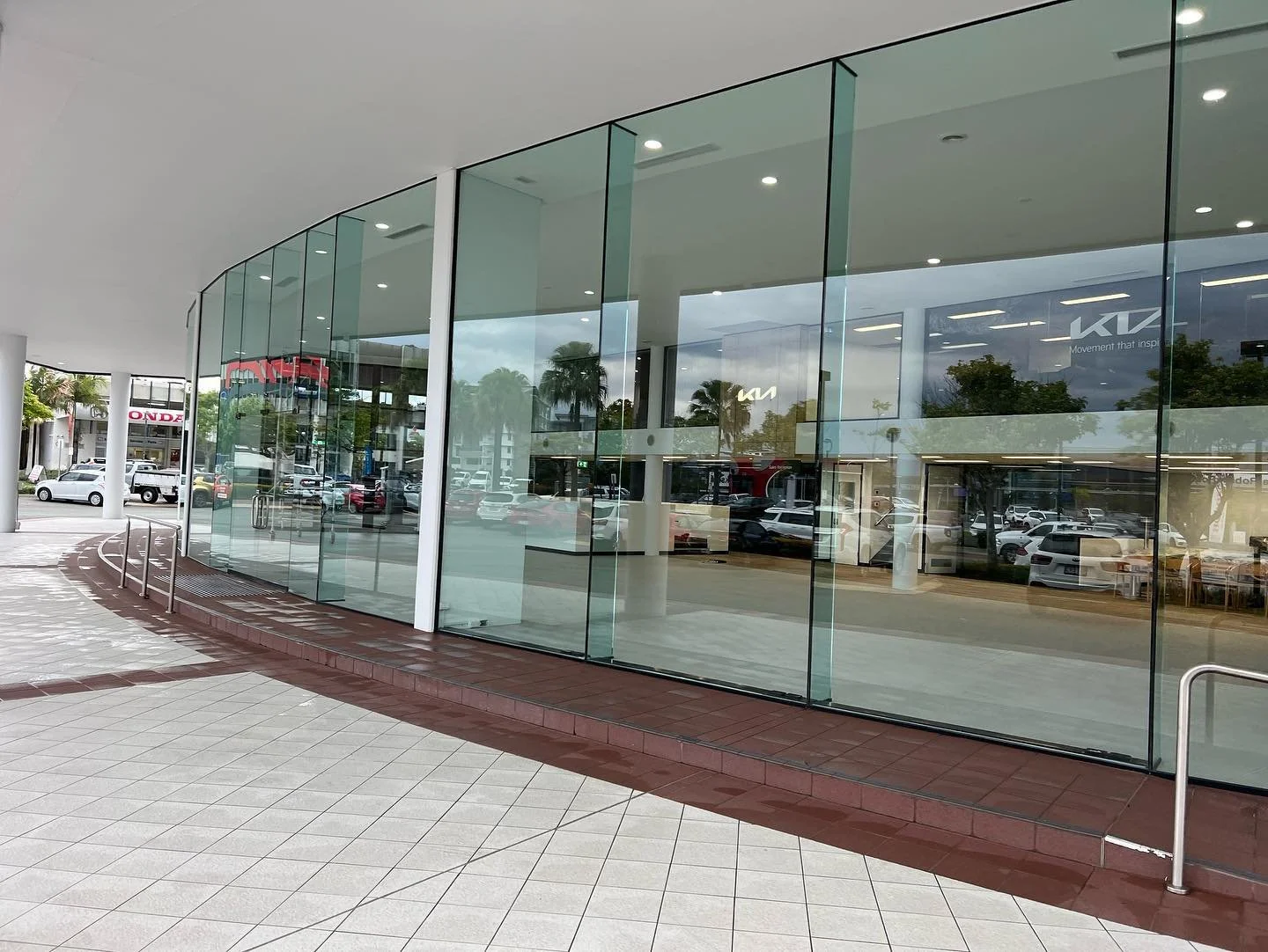 Empty car dealership with large glass windows, outdoor view showing parked cars in a lot, and a Honda logo in the background.