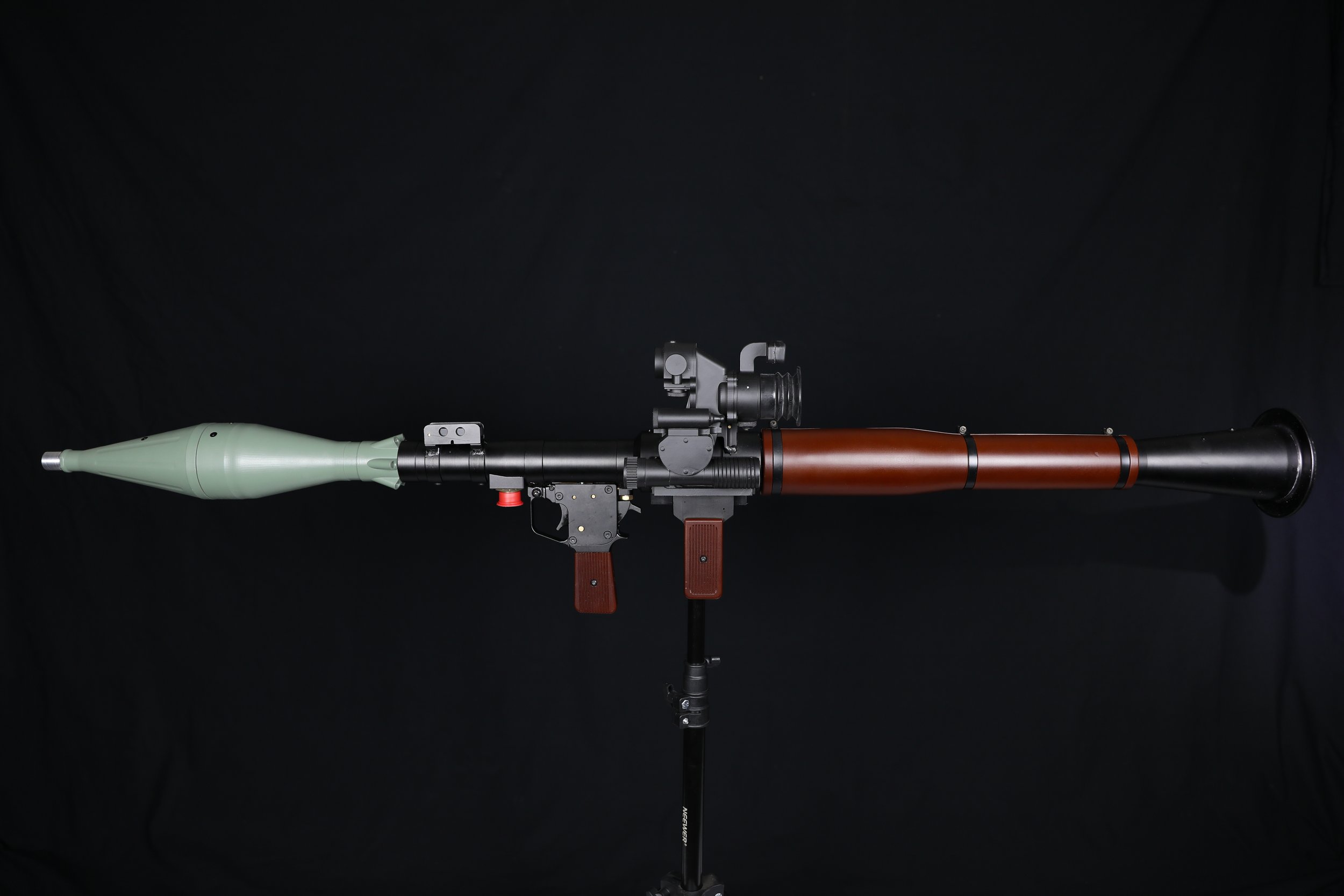 A missile with a green nose cone, mounted on a tripod against a black background.