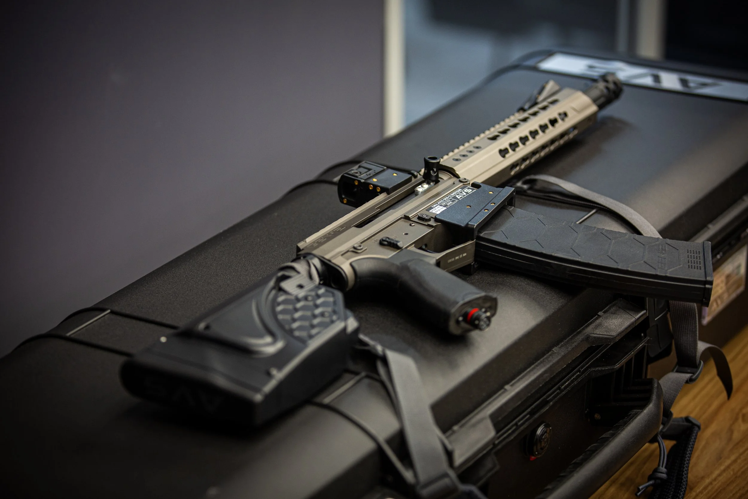 Close-up of a tactical firearm with a rail system, placed on a black surface with a smartphone and cable nearby.