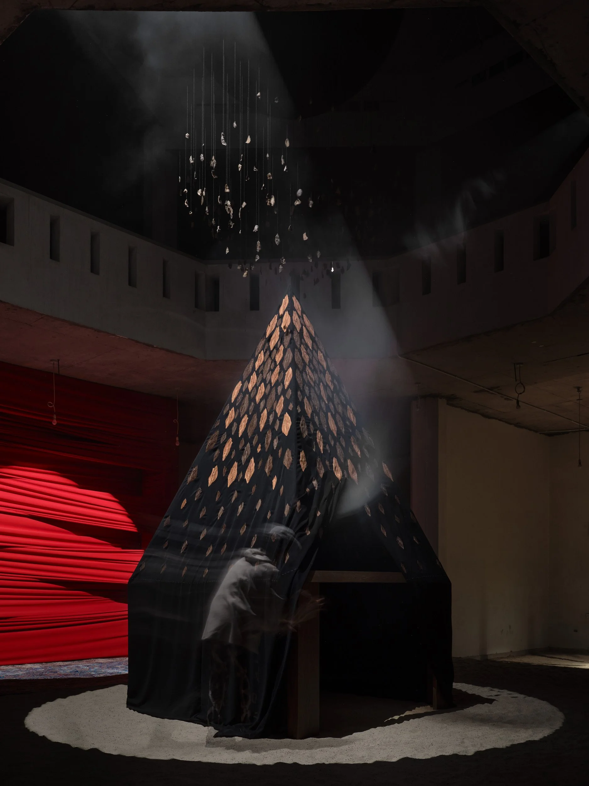 An incense burner structure fitted with abaya fabric draped across its surface, forming a membrane through which smoke is filtered and released.

Positioned at the main entrance within the atrium, the work activates the central volume of the house, w