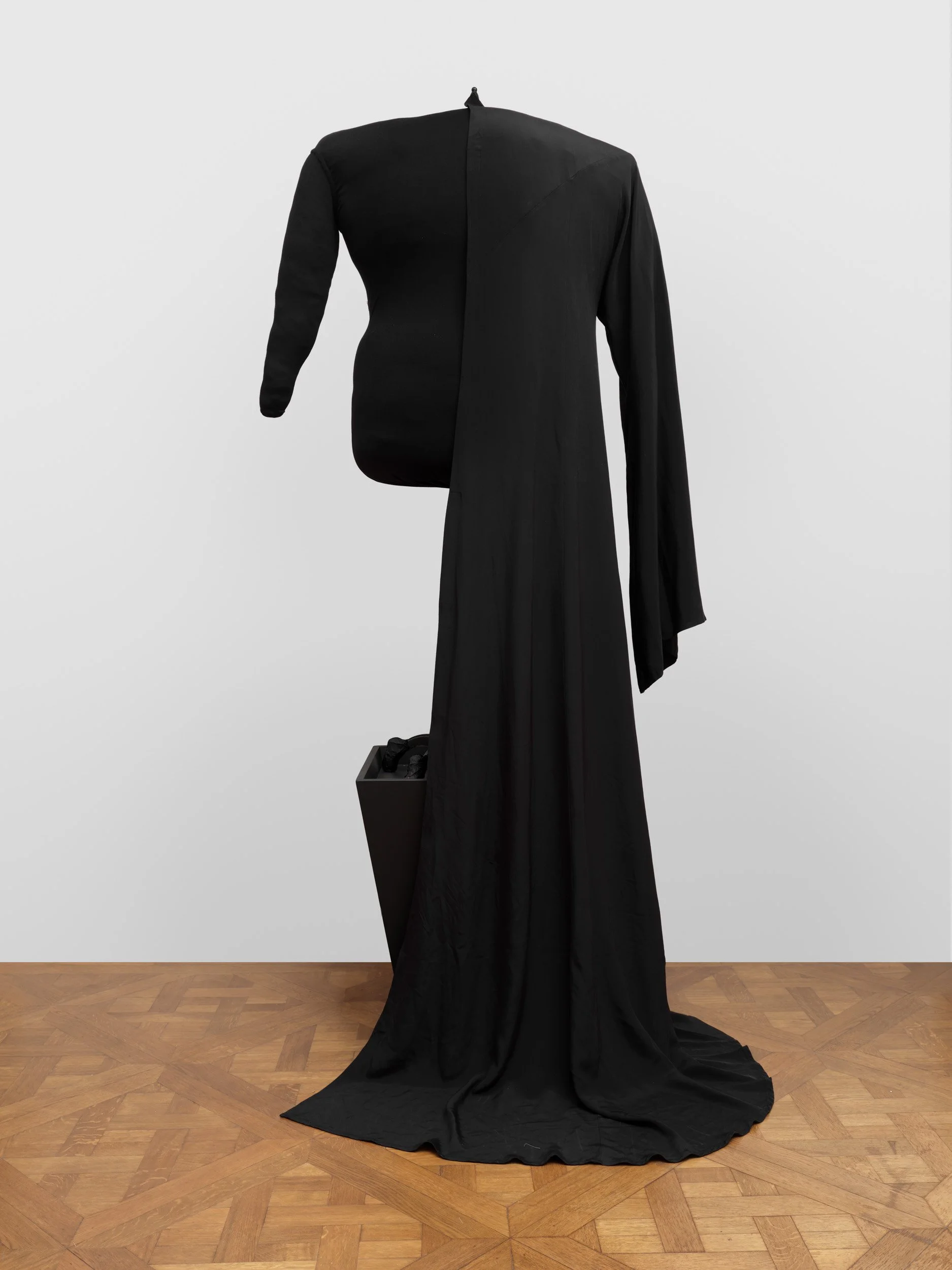 Black dress display with asymmetrical top and flowing skirt, placed on a mannequin against a white background.