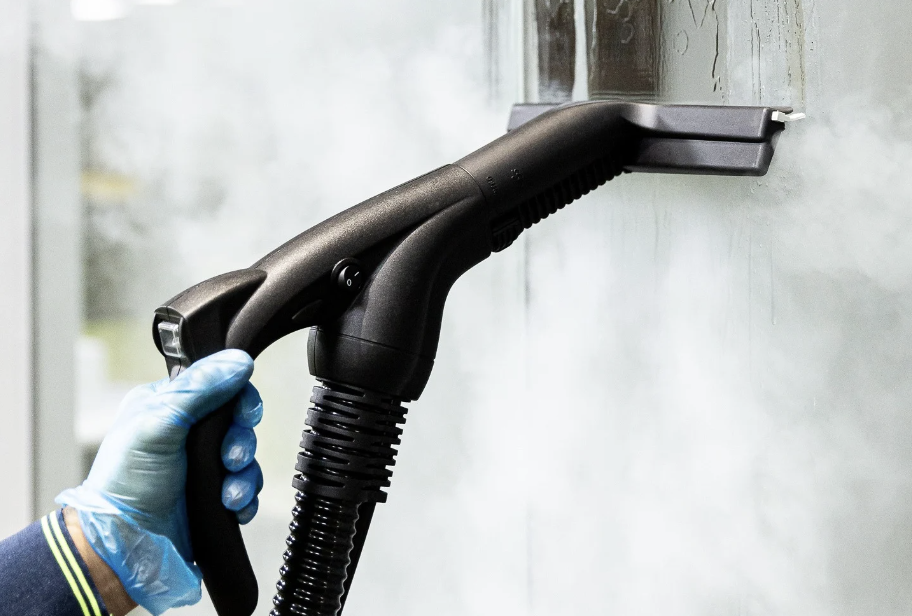 Person wearing blue gloves using a high-pressure cleaning tool on a wall.