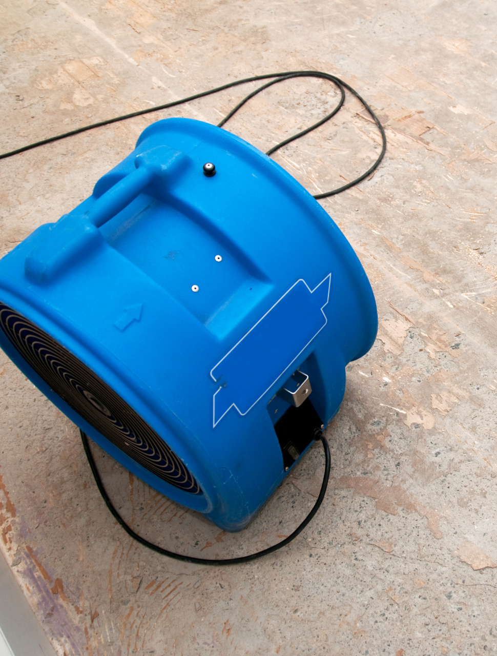 A blue portable heater with a handle on top, placed on a concrete floor. It has a power cord connected to an electrical outlet.