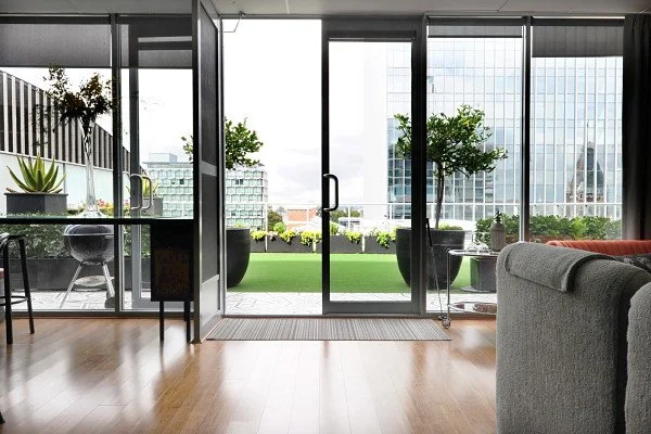 Modern living room with floor-to-ceiling glass doors leading to a balcony with potted plants and city view.