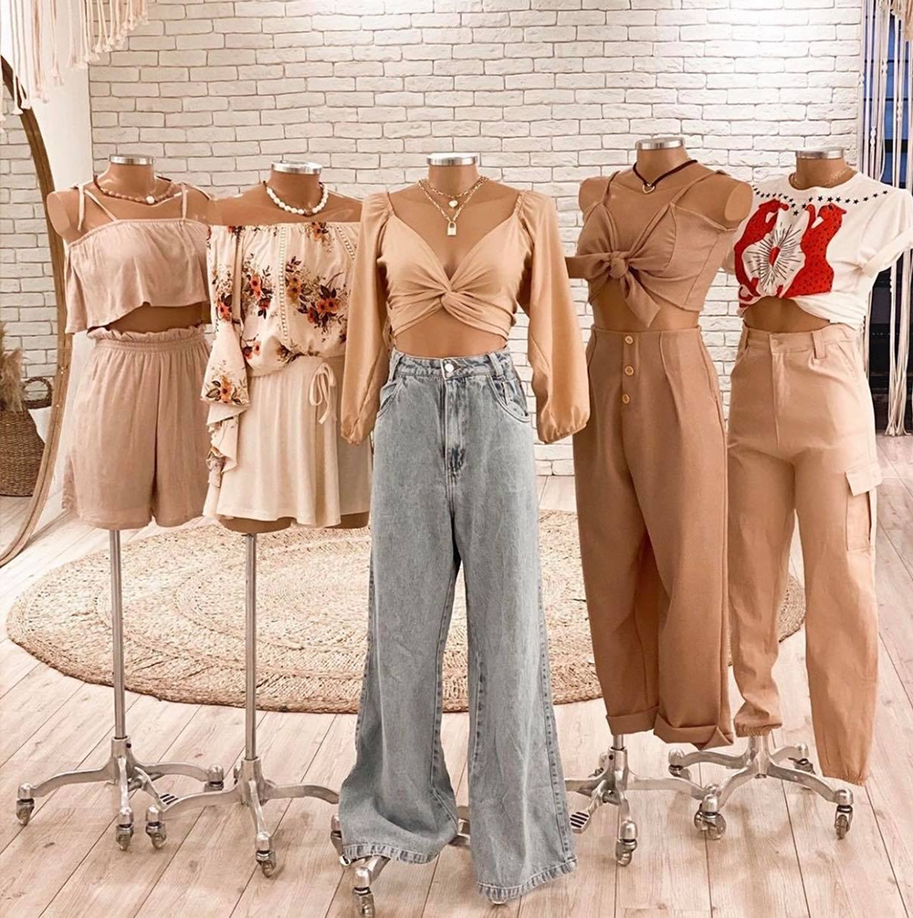 Six mannequins dressed in various beige and neutral-colored outfits, displayed in a boutique with a white brick wall background.