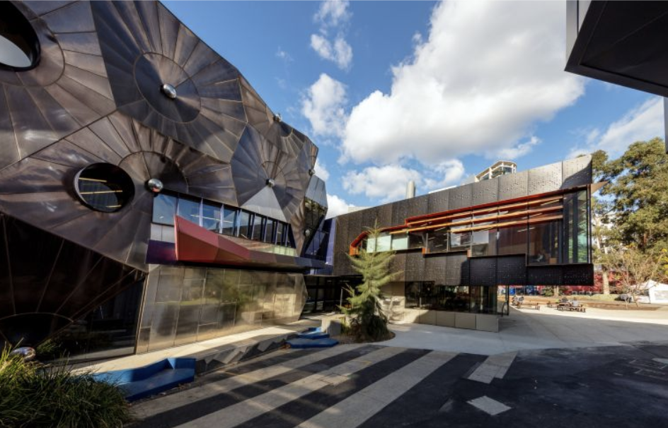 Modern architecture building with dark, metallic exterior, large glass windows, and red accent features under a partly cloudy sky.