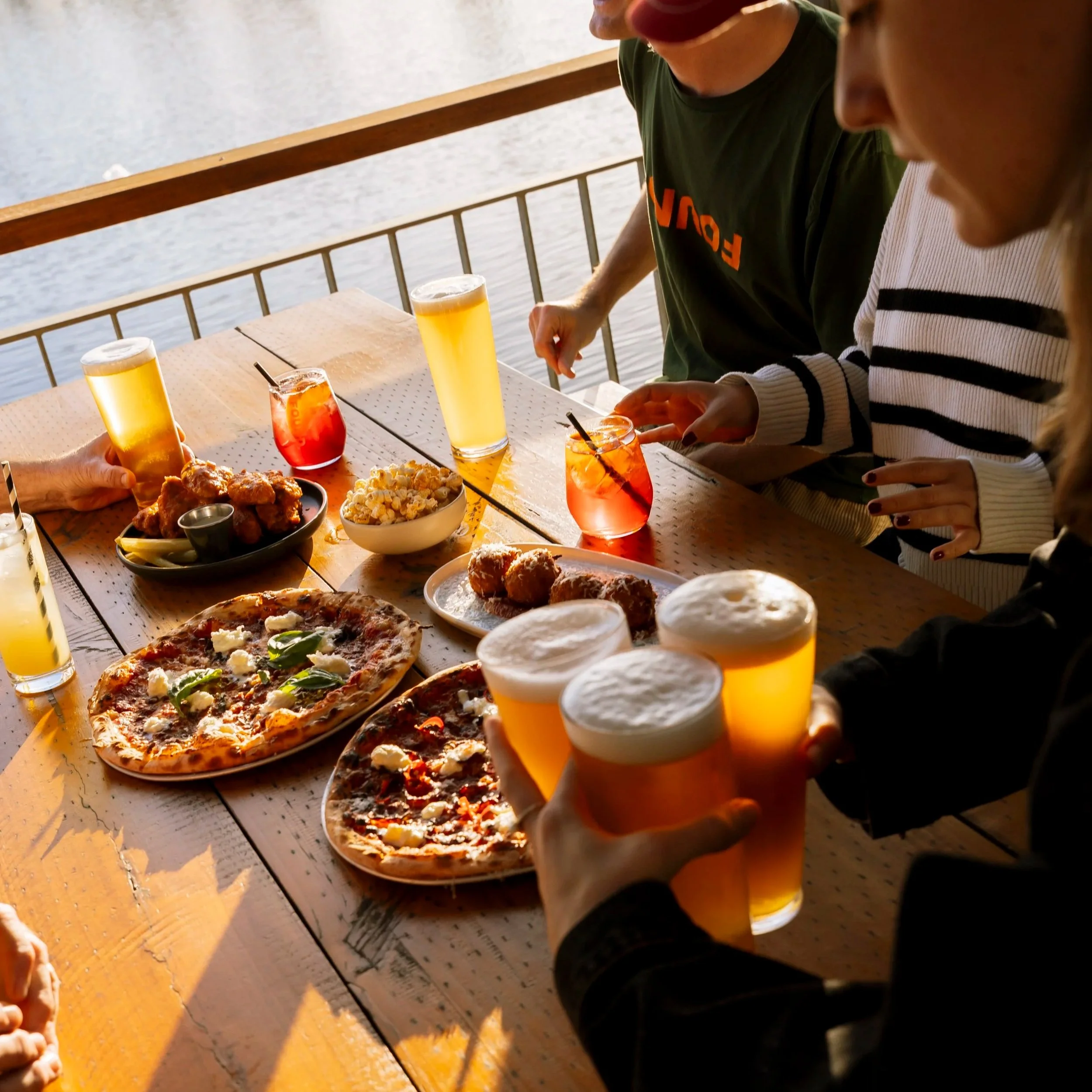 People raising pints of beers in a toast during outdoor dining by a lake in Byford at sunset