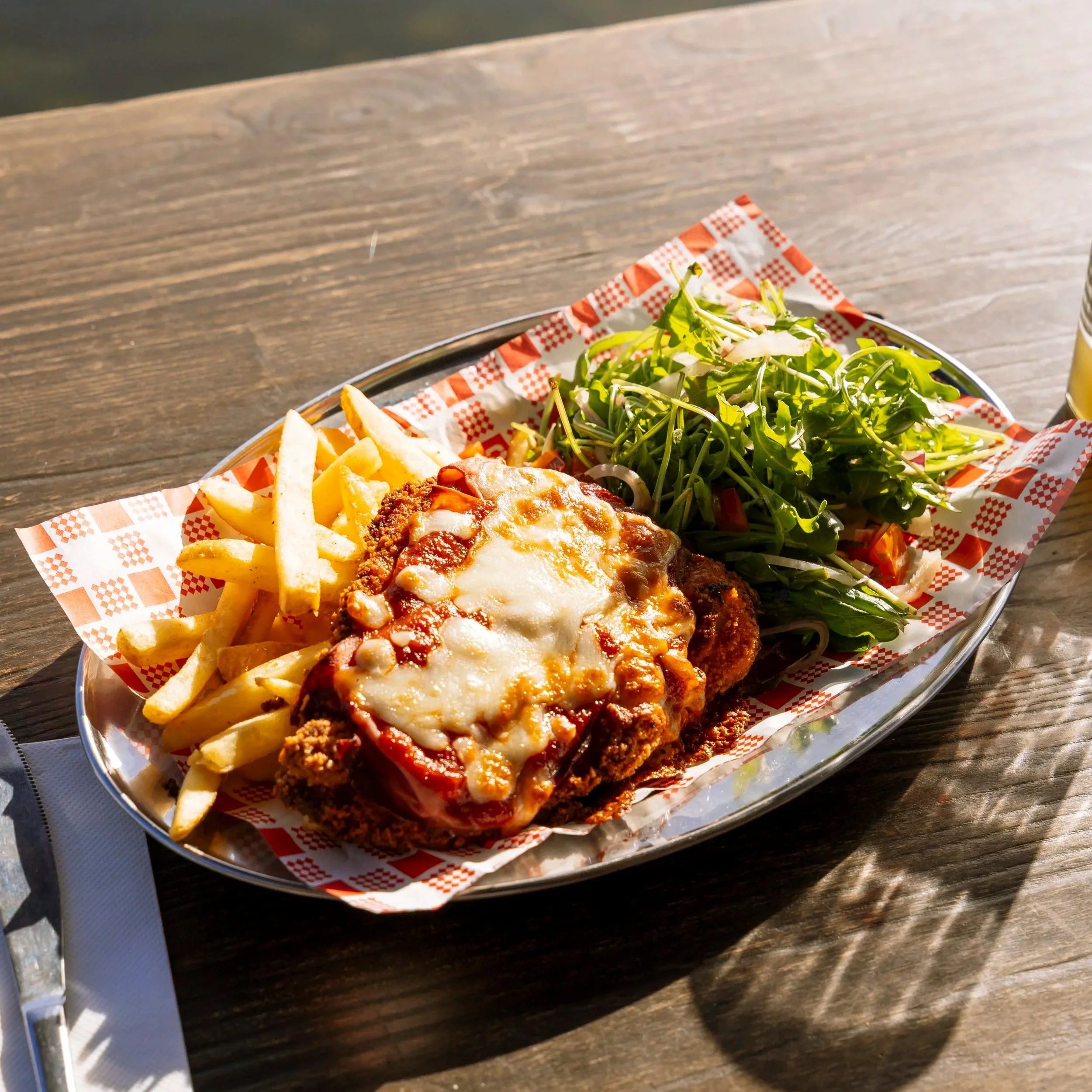 Group of friends dining, enjoying schnitzels with fries, salads, and craft beers on a wooden table.
