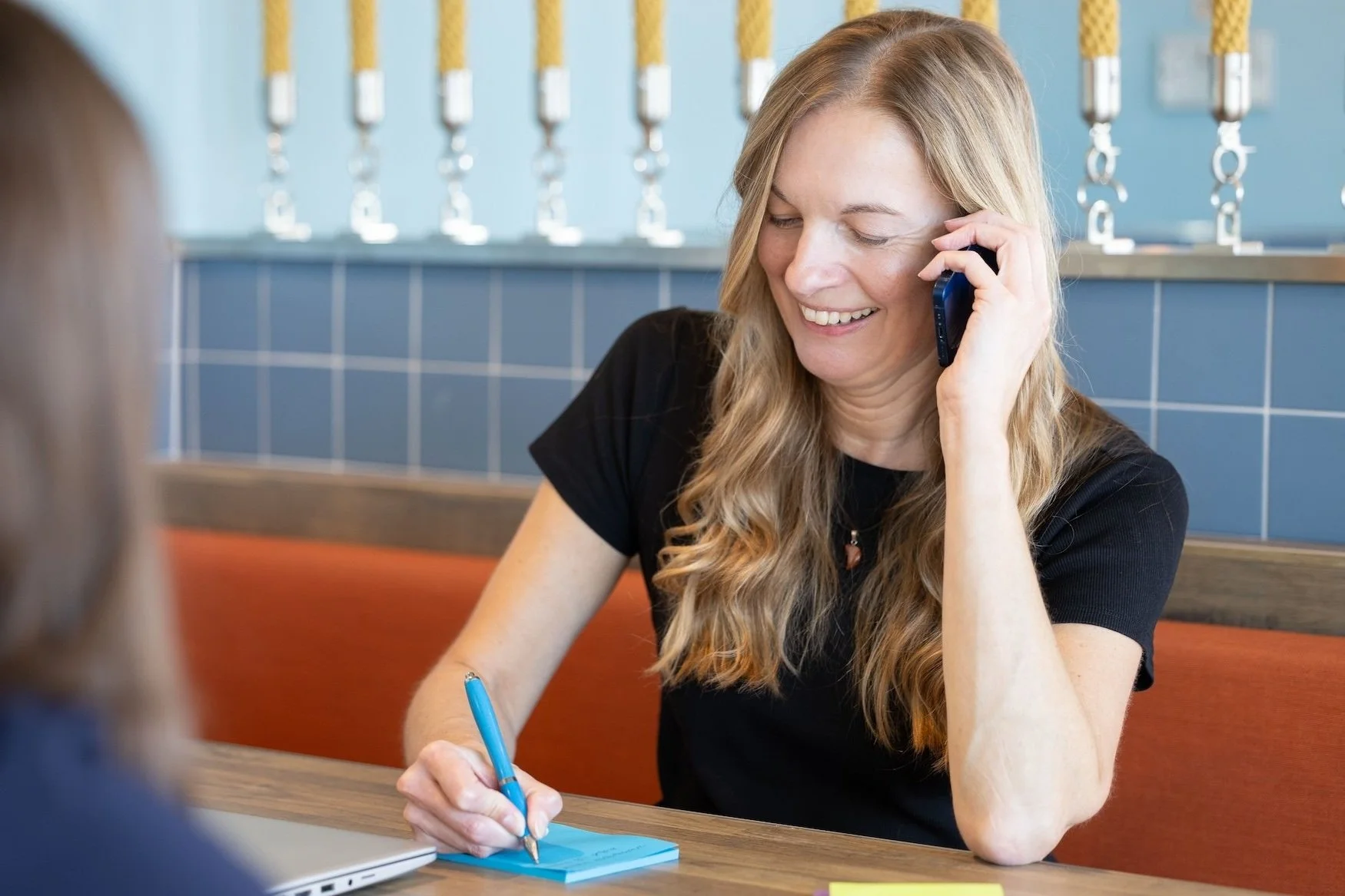 Kathy Seymour smiling, talking on phone, writing on notepad at a table.
