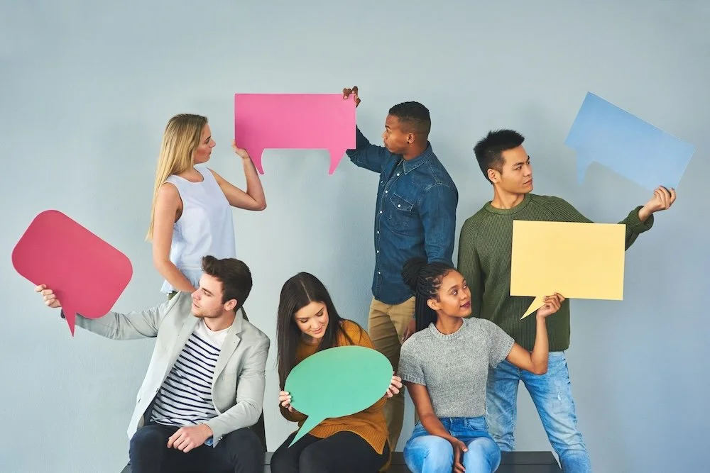 Group of six diverse people holding colorful blank speech bubble signs against a gray background.
