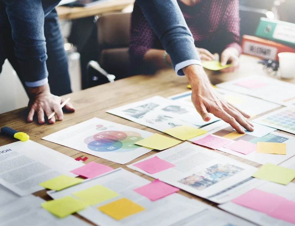 Team collaborating around a table with documents and colored sticky notes, focusing on a business plan and creative ideas.