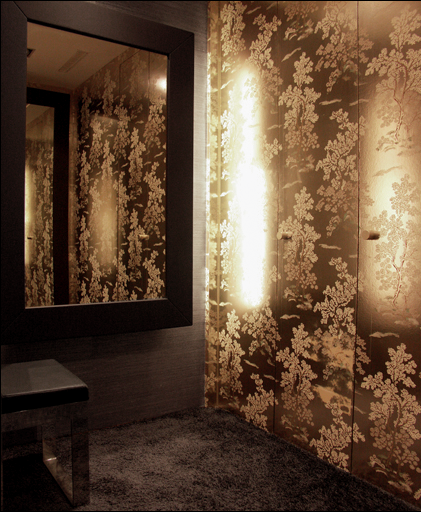 A corner of a room with a large wall mirror, floral wallpaper, a small bench, and a textured carpet.