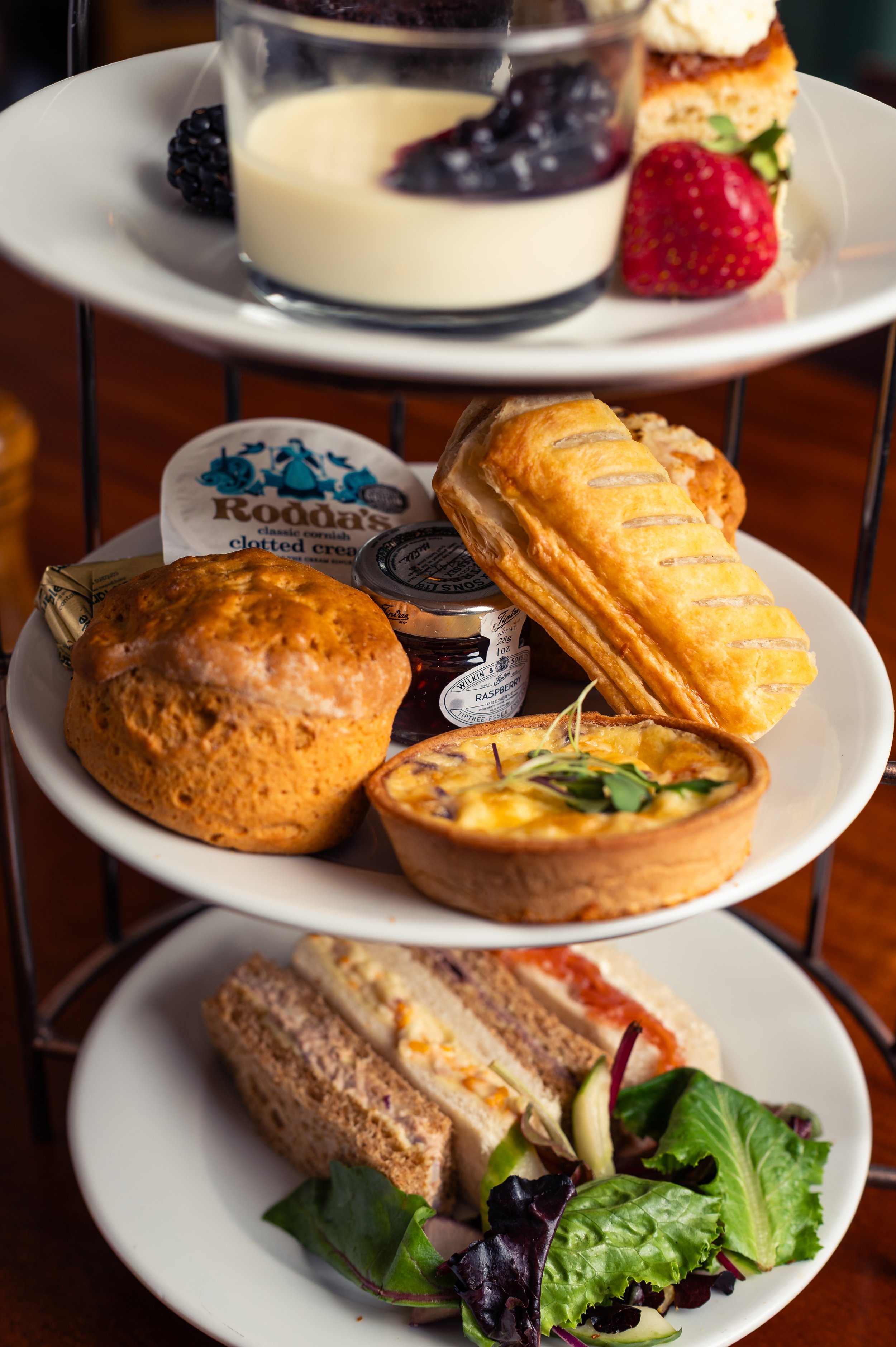 A three-tiered serving tray with assorted desserts, pastries, and a sandwich with a side salad.