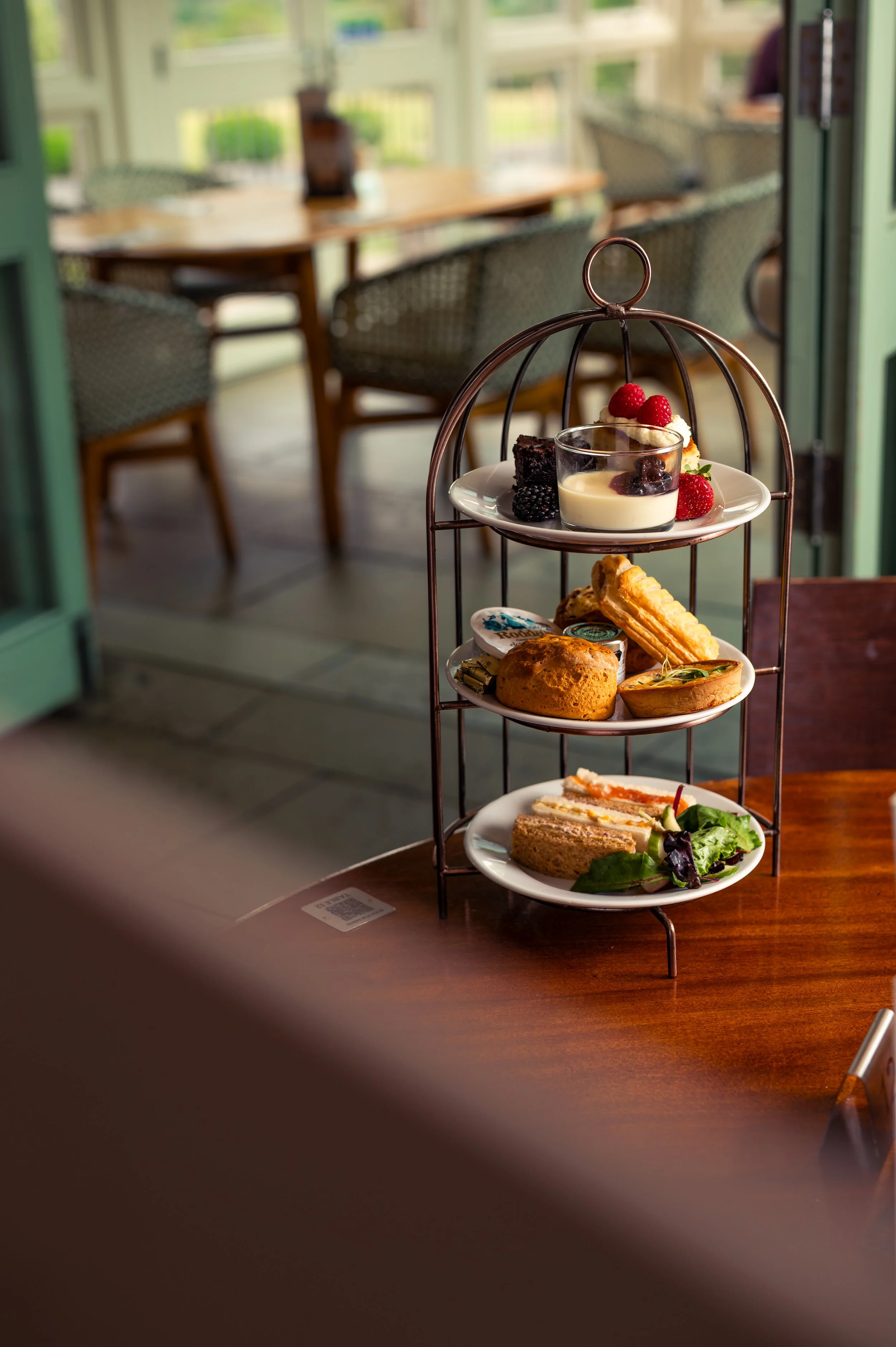A three-tiered serving stand with assorted desserts and finger foods in a bright cafe or restaurant setting.