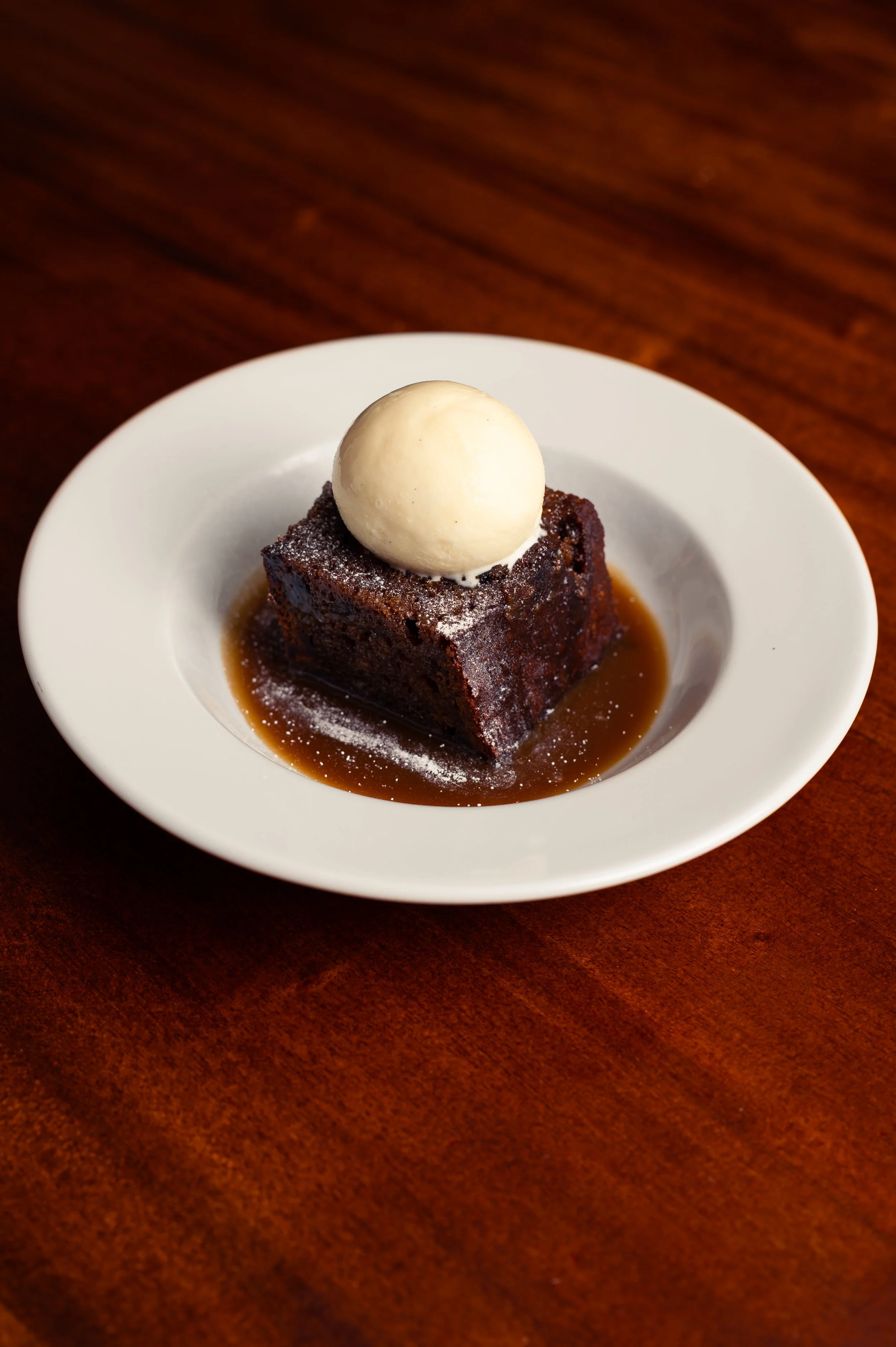 Chocolate dessert with a scoop of vanilla ice cream on top, served in a white bowl on a wooden table.