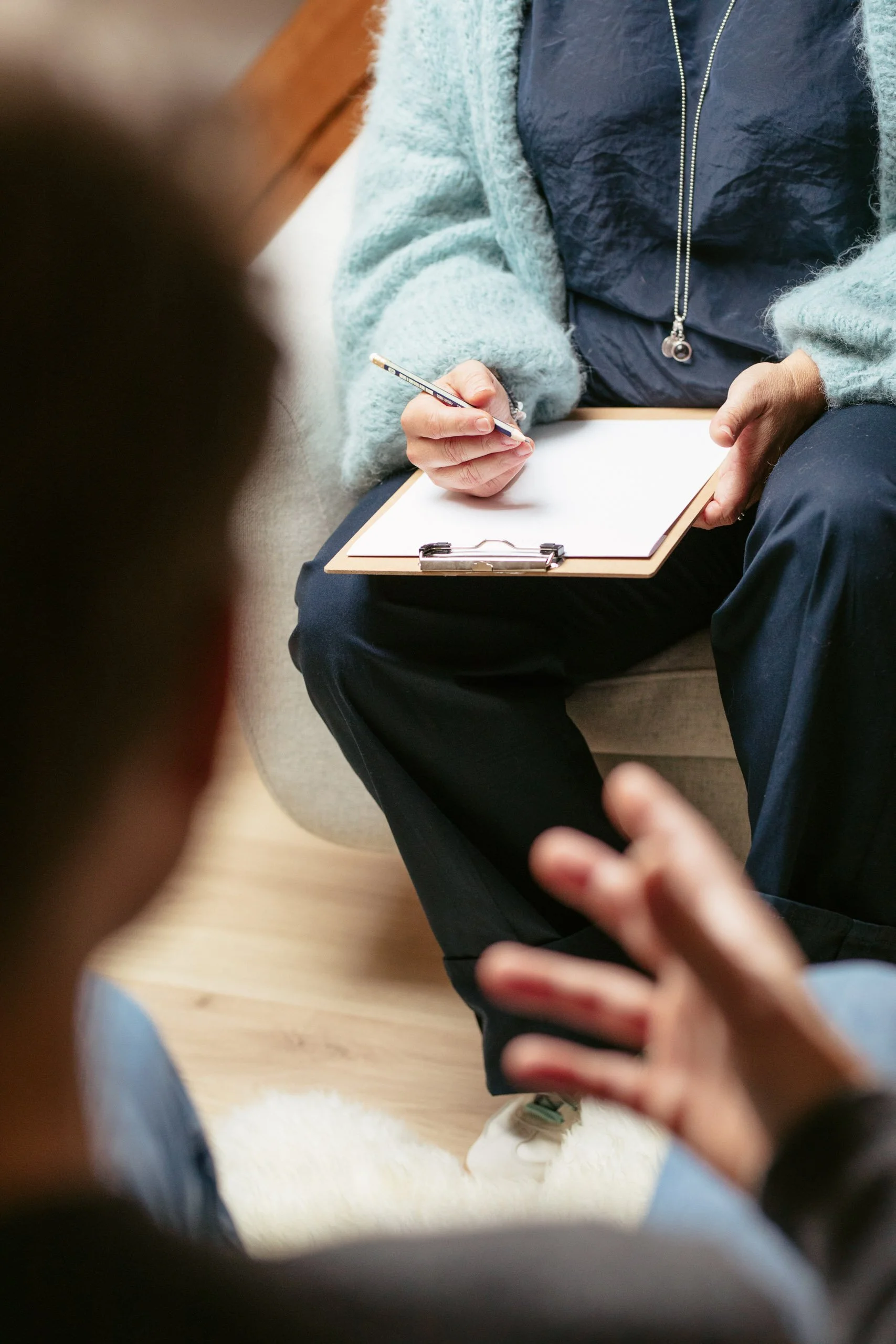 Jemand schreibt auf ein Whiteboard während eines Gesprächs, im Vordergrund sind zwei weitere Personen sichtbar.