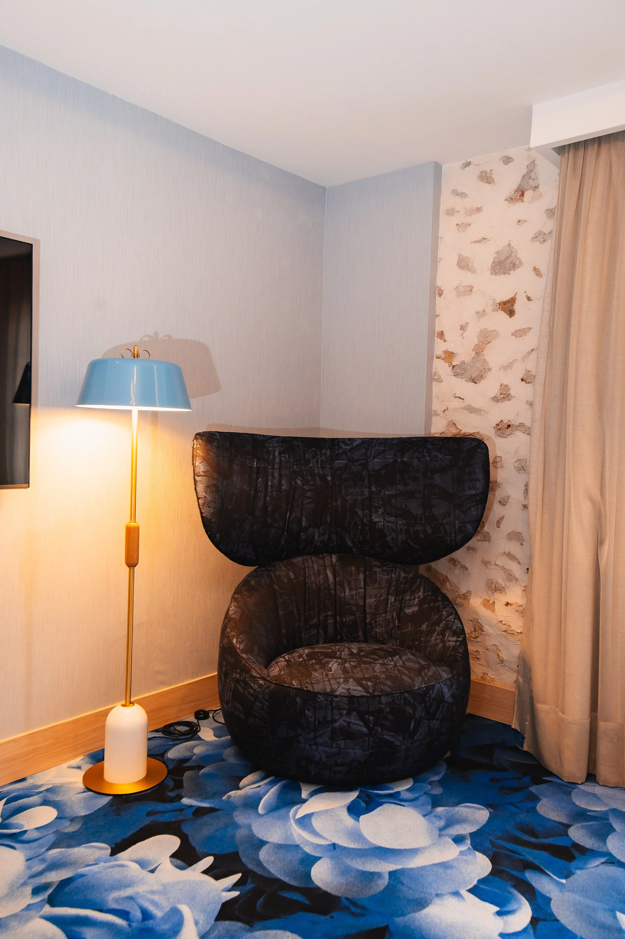 Sillón en forma de cabeza de perro con una lámpara de pie y cortinas en una habitación decorada con paredes de piedra y papel tapiz azul.