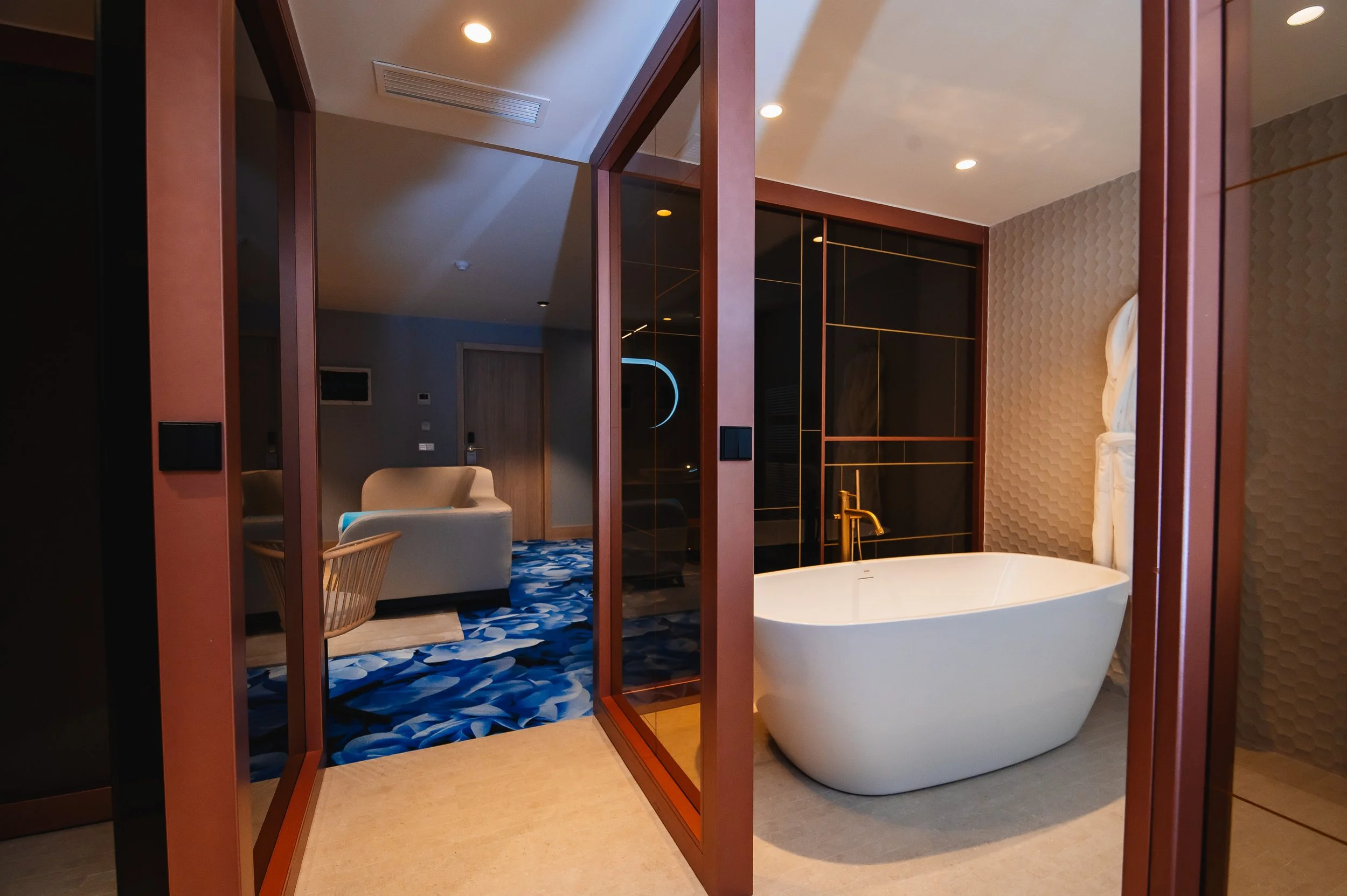 Una habitación moderna con una bañera, repartido en dos áreas, con paredes de texturas diferentes y un ambiente elegante y bien iluminado