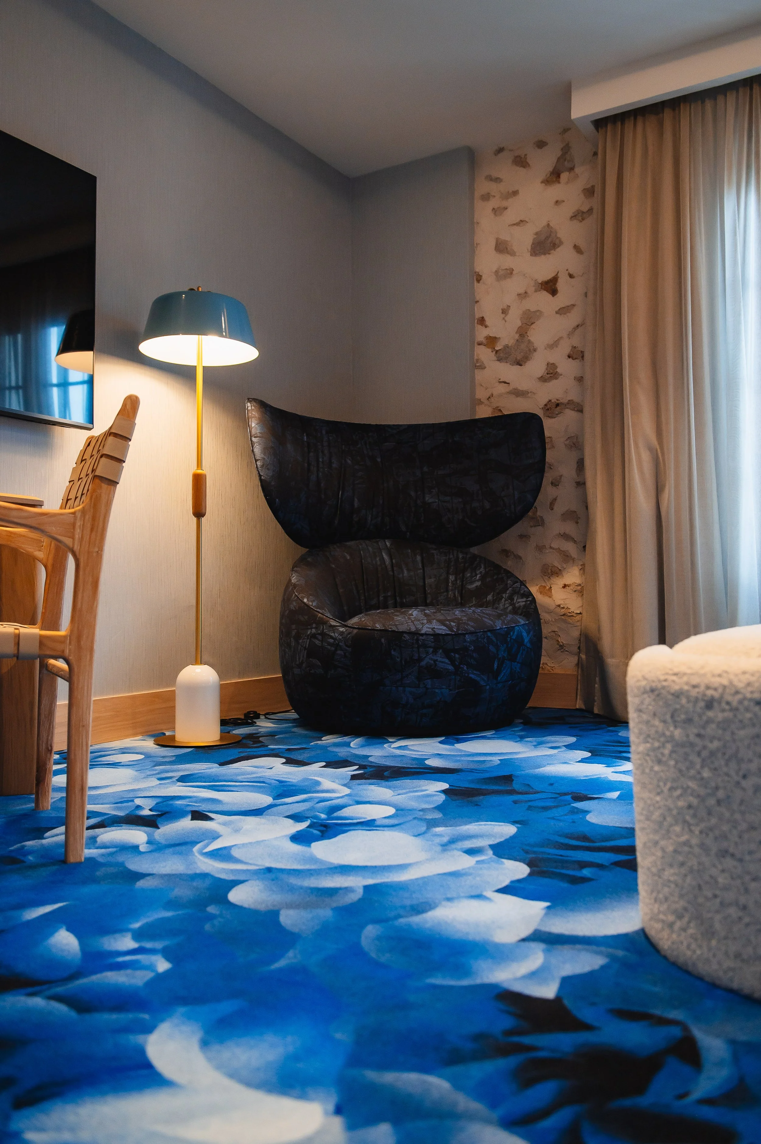 Sofá negro en forma de capullo en una habitación con cortinas beige y lámpara de pie azul y dorada.