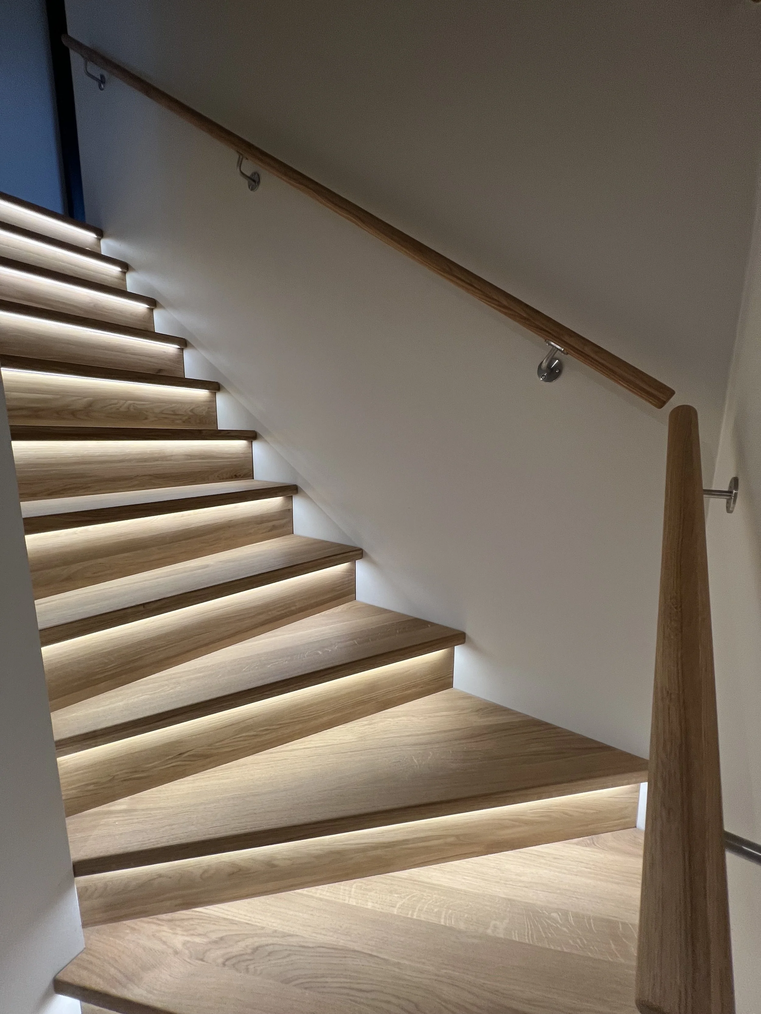 Trappe med trægulv og håndløber, oplyst med LED-lys under trinene.