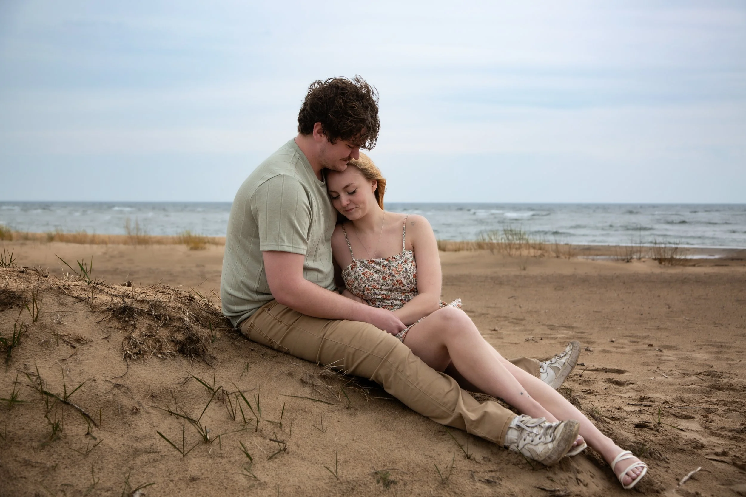 A young couple sitting on the sandy beach, embracing each other with the ocean in the background.