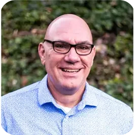 Smiling man with glasses in a blue shirt outdoors