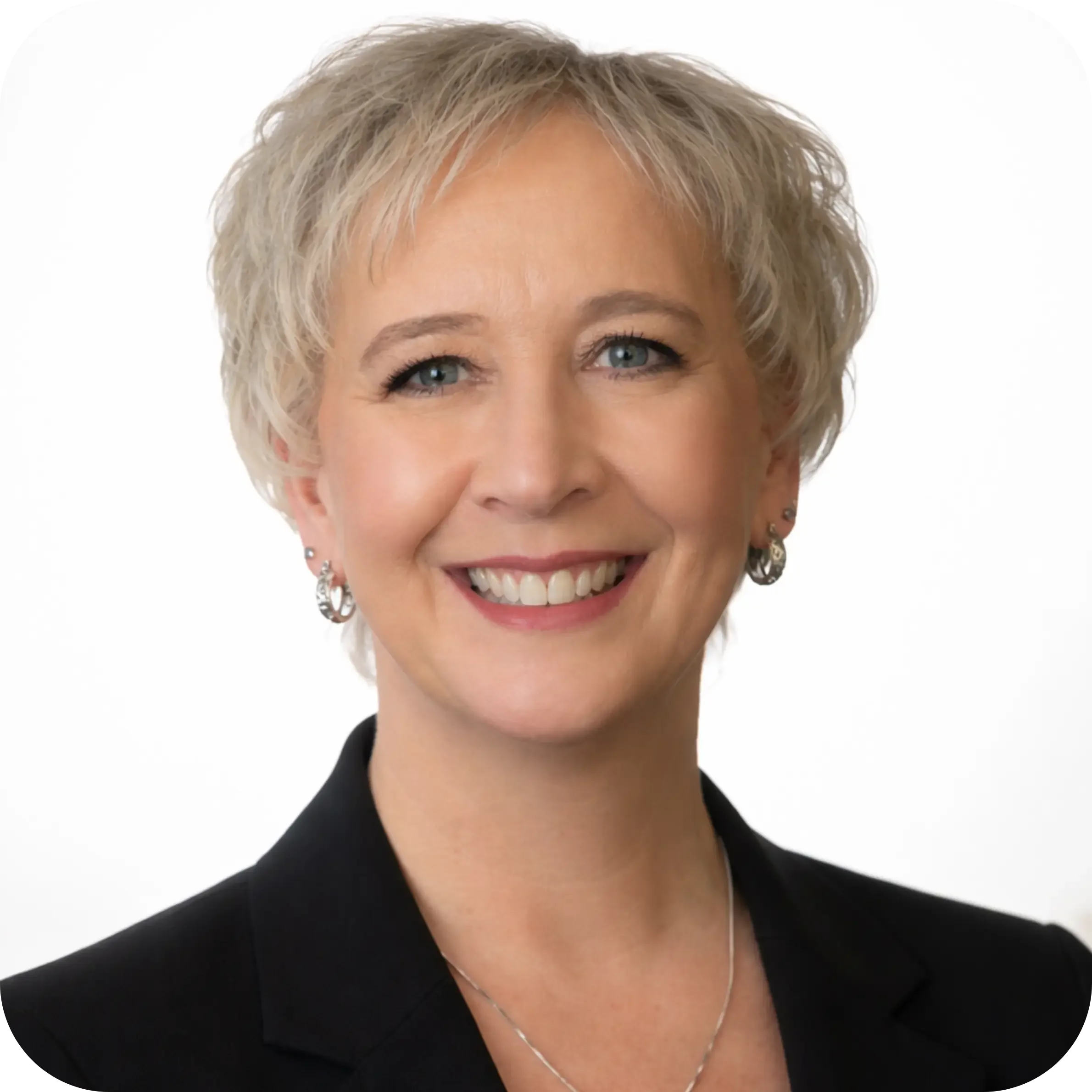A woman with short blonde hair smiling, in an indoor setting with blurred background including a bicycle.