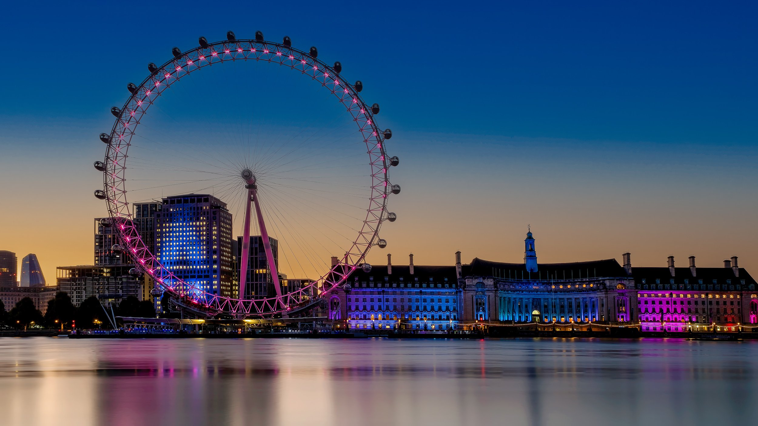 Sunrise photo of the London Eye with blue and orange sky and a smooth silky water on the River Thames.
