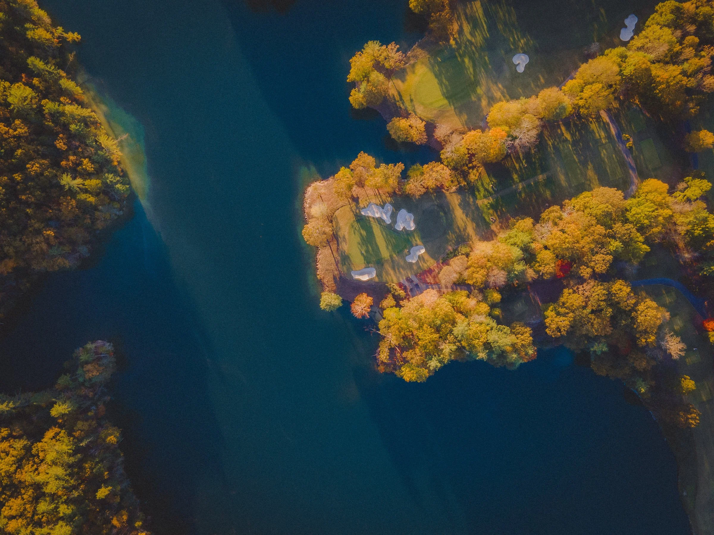 Aerial view of a lake with a small golf course on one side, surrounded by colorful autumn trees.
