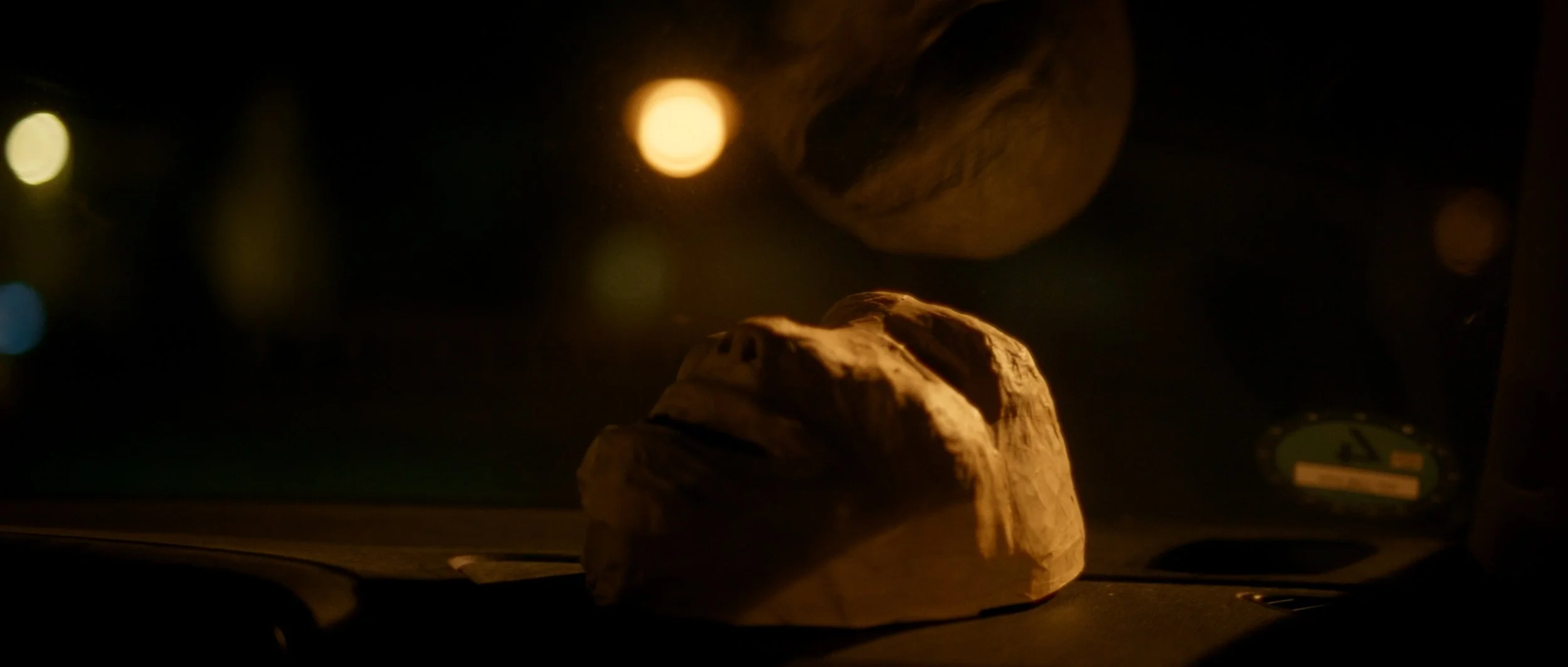 Eine Maske auf einem Armaturenbrett bei Dunster Nacht, mit verschwommenen Lichtern im Hintergrund.