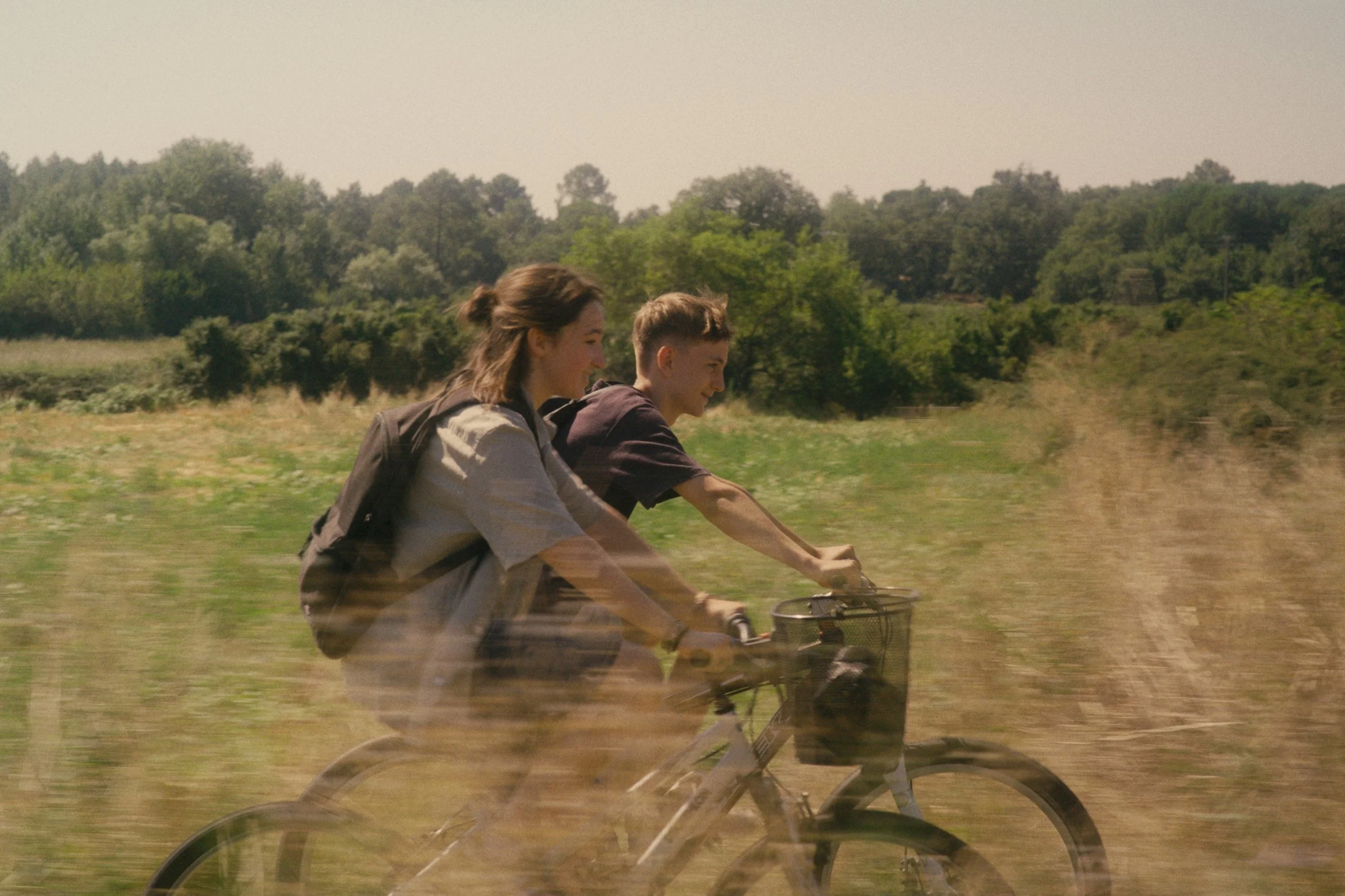 Zwei Jugendliche fahren Fahrrad auf einer landlichen Strecke bei sonnigem Wetter.