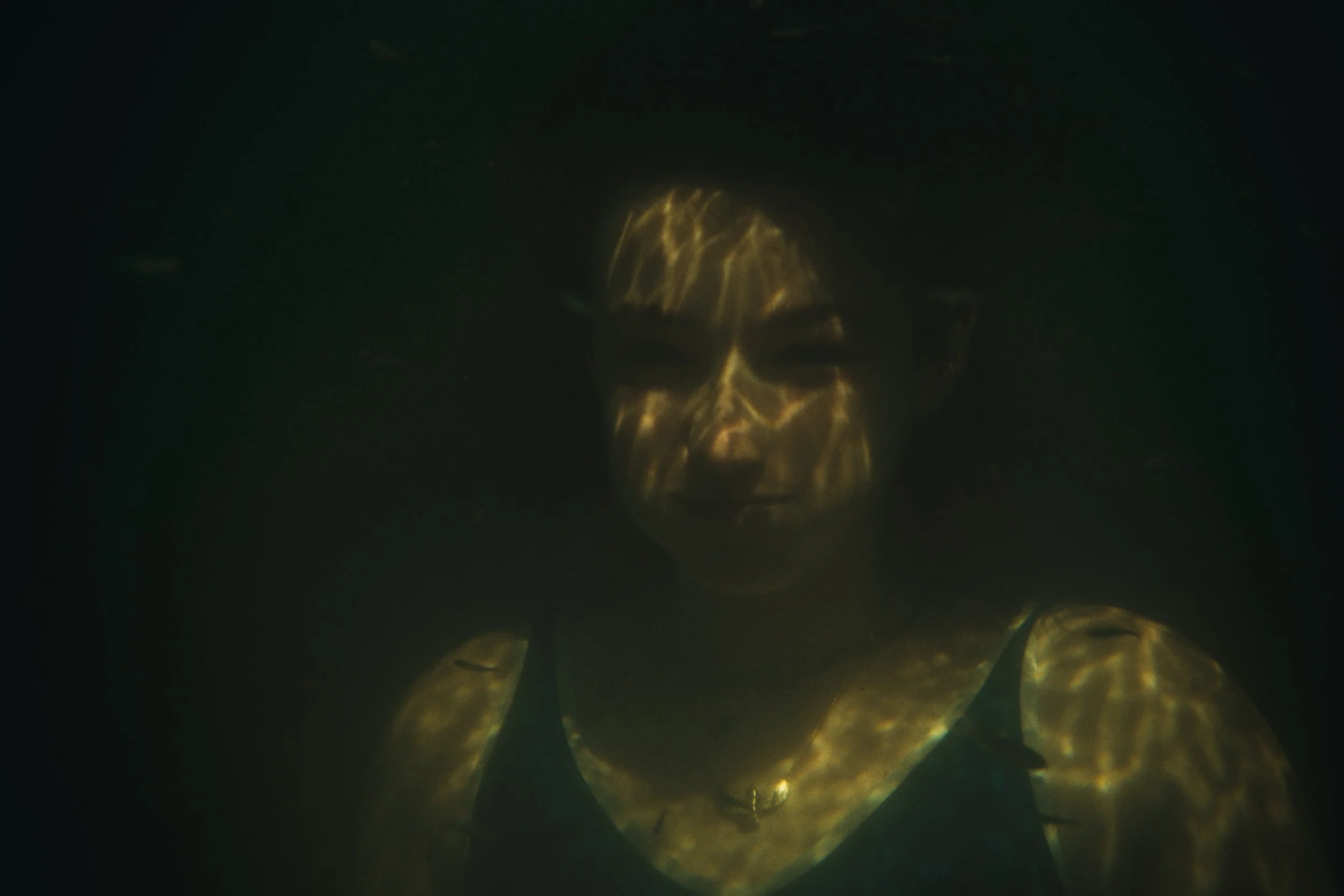 Eine Person schwimmt im Dunkeln, ihr Gesicht ist teilweise vom Wasser bedeckt und durch Lichtreflexe verzerrt.