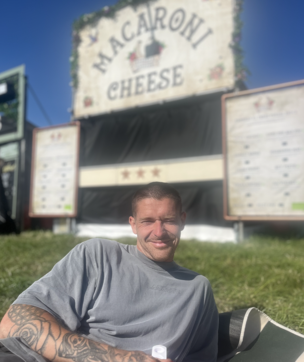 Dan smiling in front of the macaroni cheese stall at Glastonbury 2025