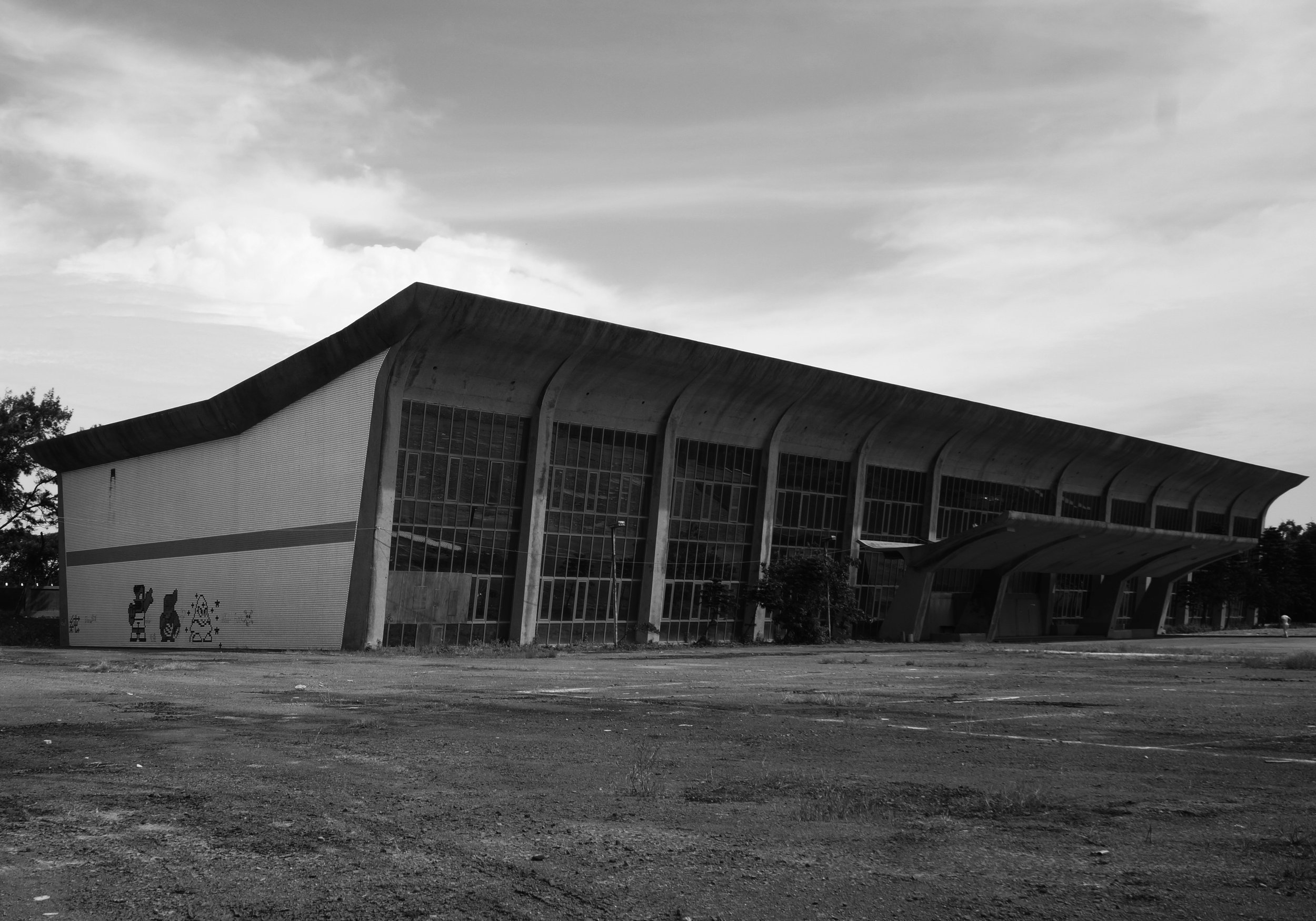 A black and white photo of a building in ruins, built with concrete on the sides and long glass windows in the front