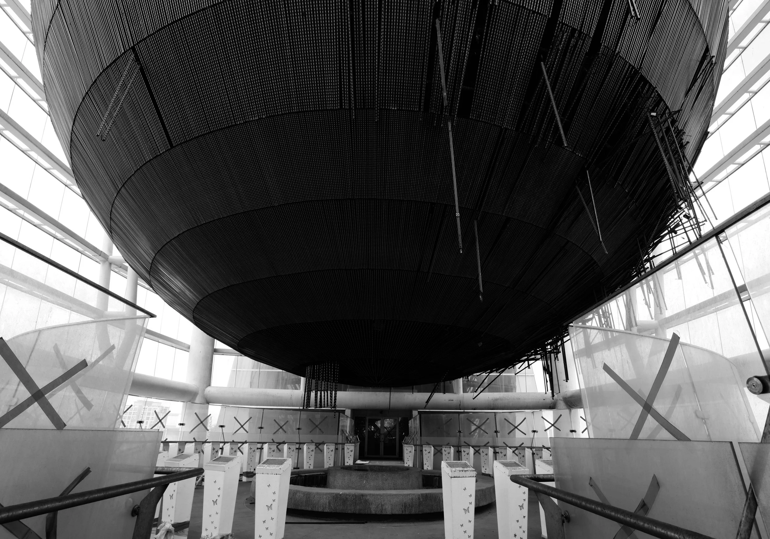 A black and white photo of the inside of a ruined building. There is a metal dome structure in the middle, surrounded by short pillars.