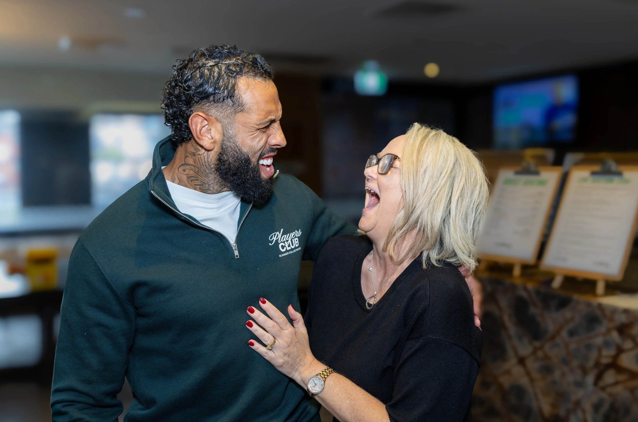 A man and a woman sharing a joyful moment, smiling and laughing, in an indoor setting.