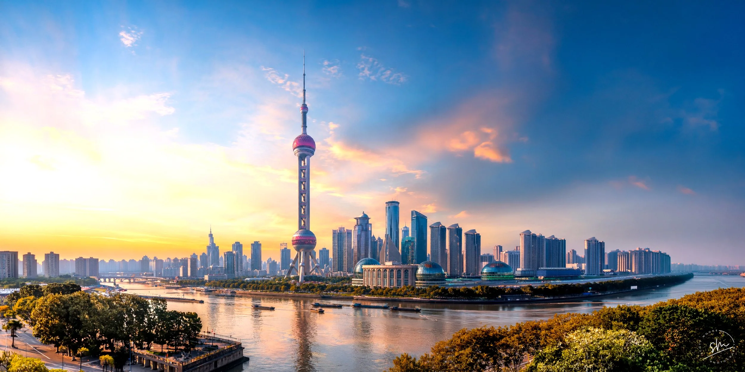 Shanghai skyline with the Oriental Pearl Tower at sunset, showcasing city buildings along the river.