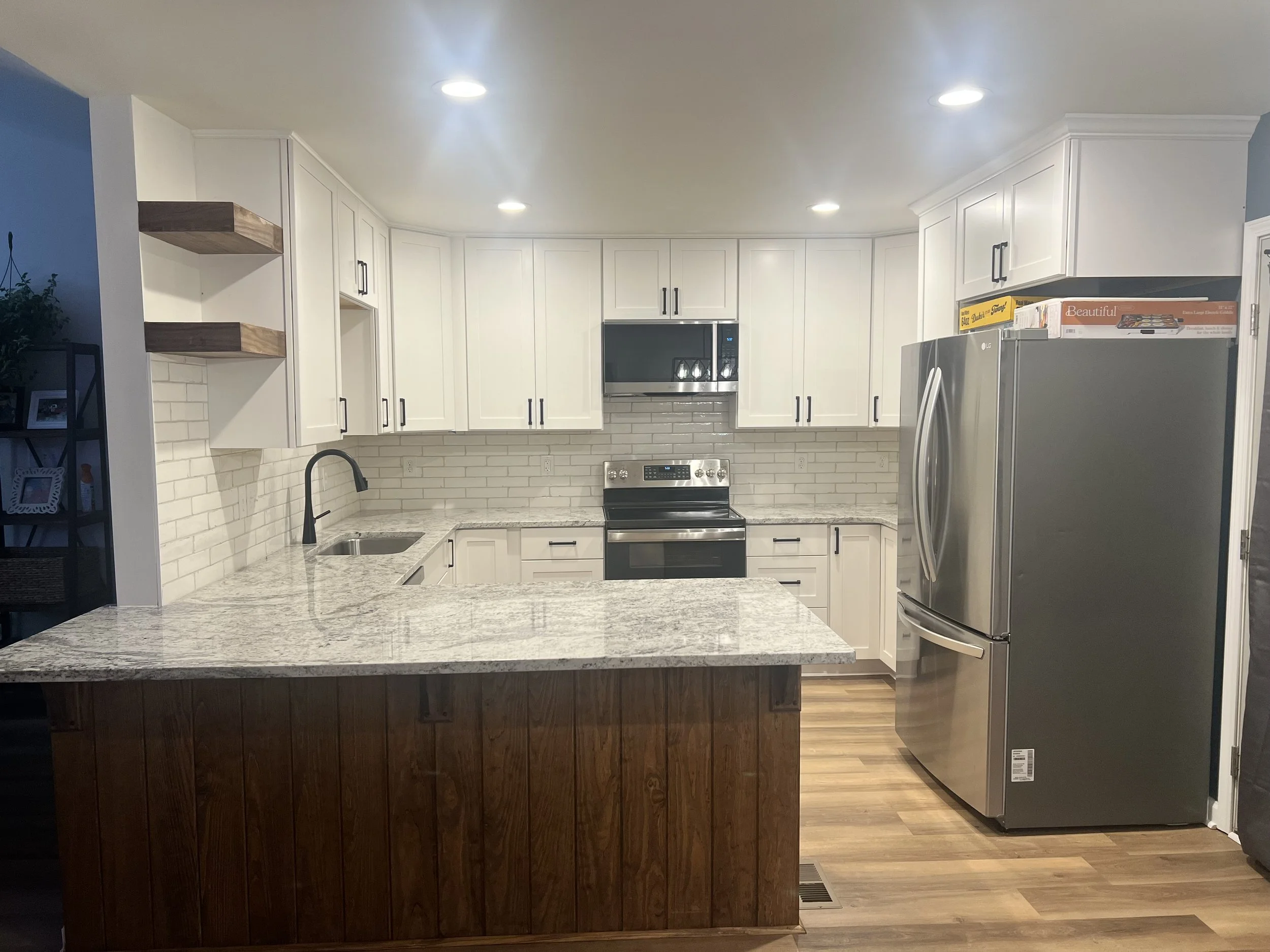 Full kitchen remodel featuring custom shaker-style cabinets with sleek black finishes, custom shelving, a stained shiplap bar, and premium granite countertops. - Zebulon, NC