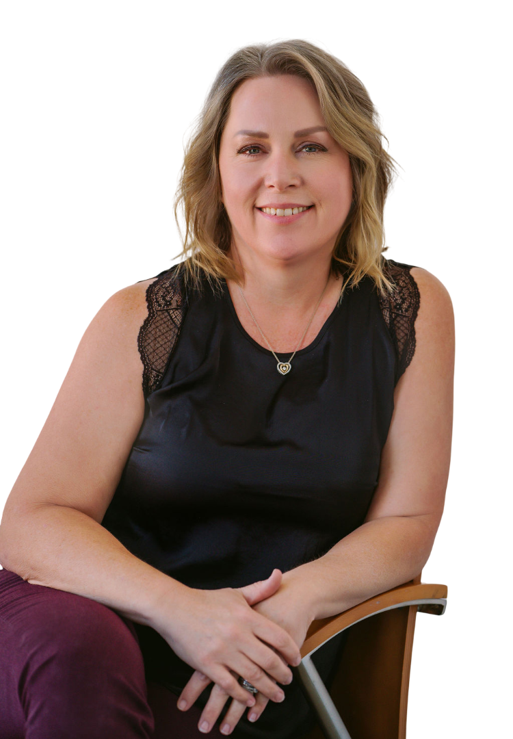 A woman with shoulder-length blonde hair, wearing a black sleeveless top with lace details on the shoulders, smiling and sitting on a wooden chair with crossed hands.
