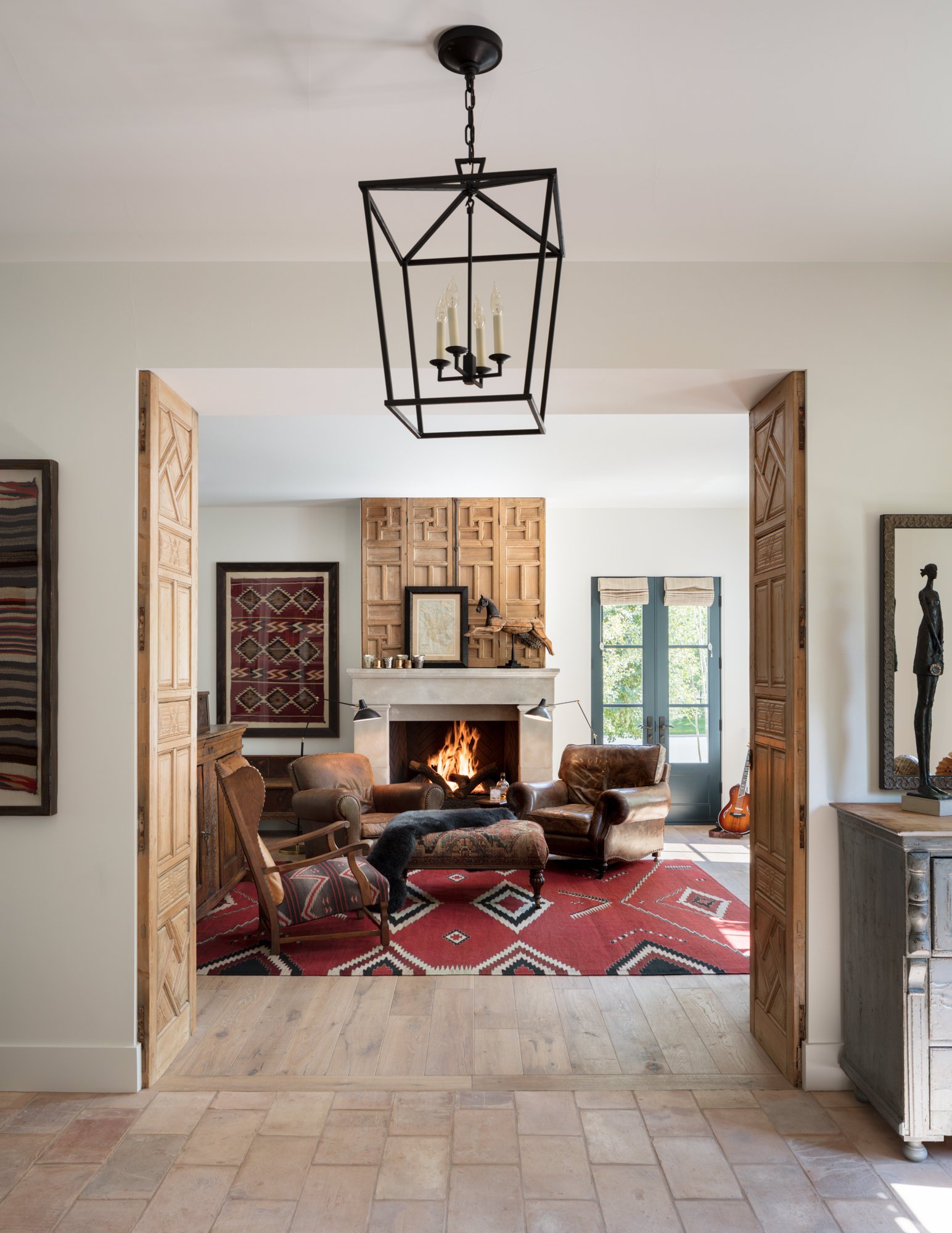Living room with a fireplace, leather chairs, a red patterned rug, and wooden sliding doors.