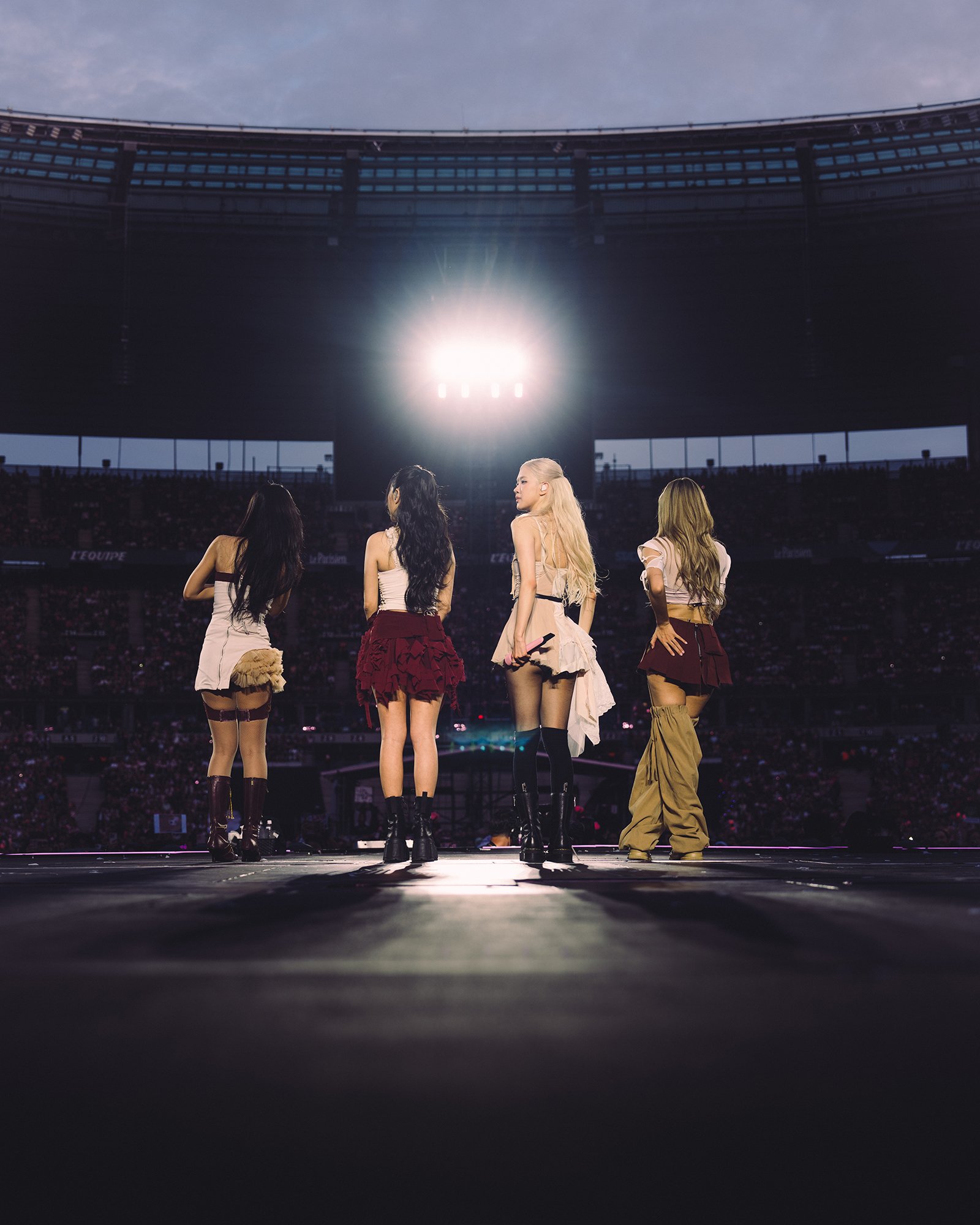 Four women performing on a stage in a stadium, with a bright light shining behind them.
