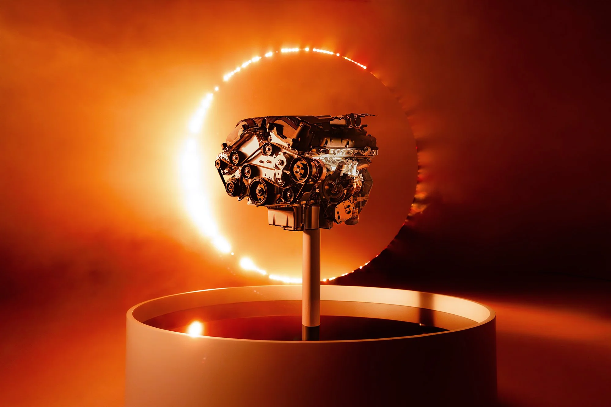 A metallic engine mounted on a stand in front of a fiery circular background.