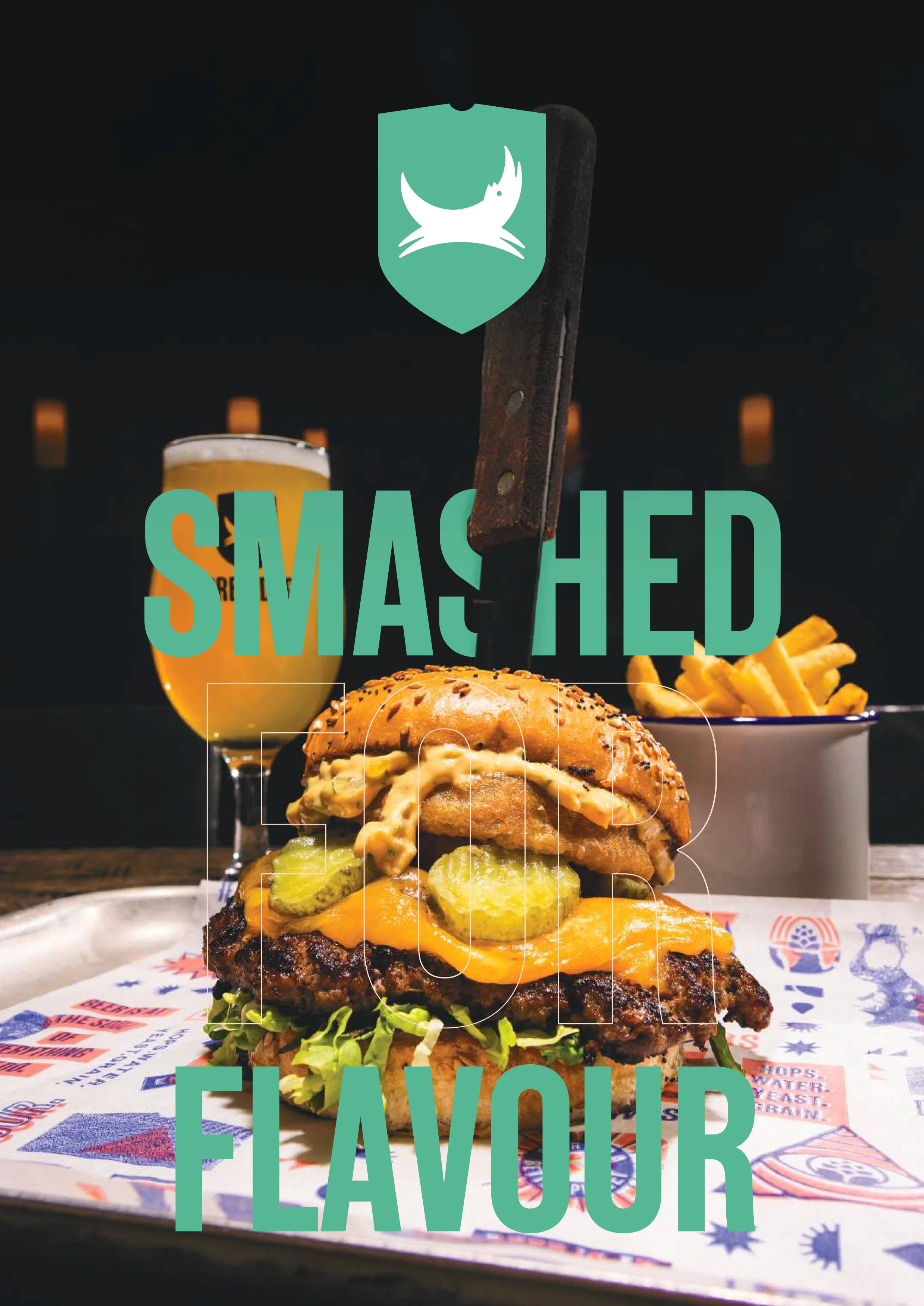 A burger with pickles, cheese, lettuce, and sauce, served on a paper tray. In the background, a glass of beer and a cup of french fries. Text overlay reads "Smashed for Flavour".